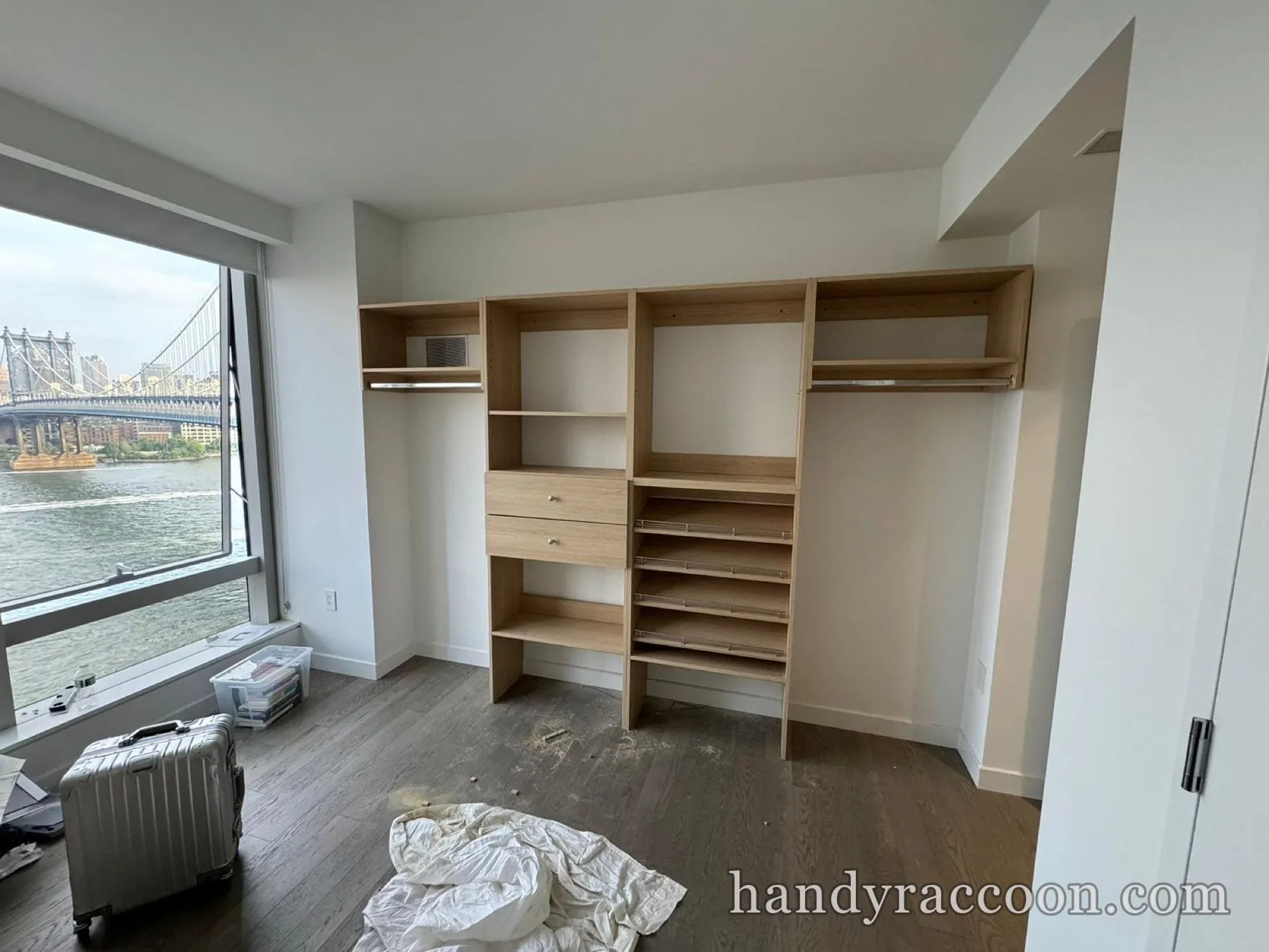 Light wood closet organizer with drawers, hanging rails and angled shoe shelves in a bright bedroom
