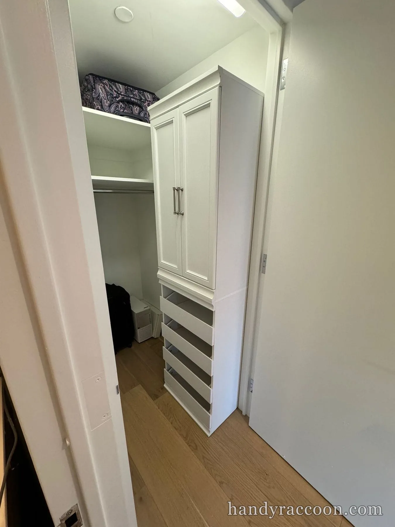 White closet cabinet unit with upper doors and open drawers inside a narrow reach-in closet