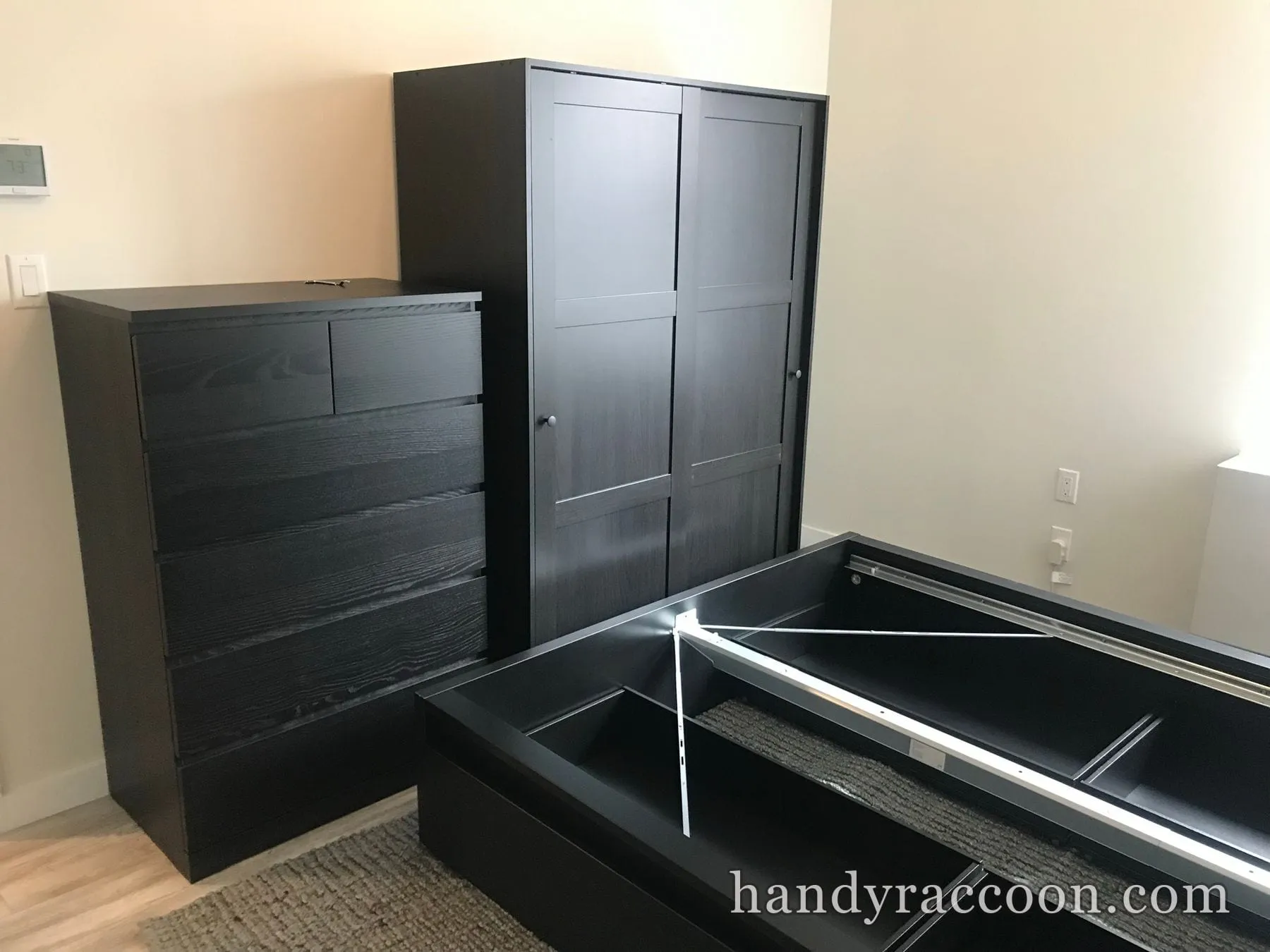 Black chest of drawers and dark wardrobe assembled in a bedroom with a bed frame under assembly