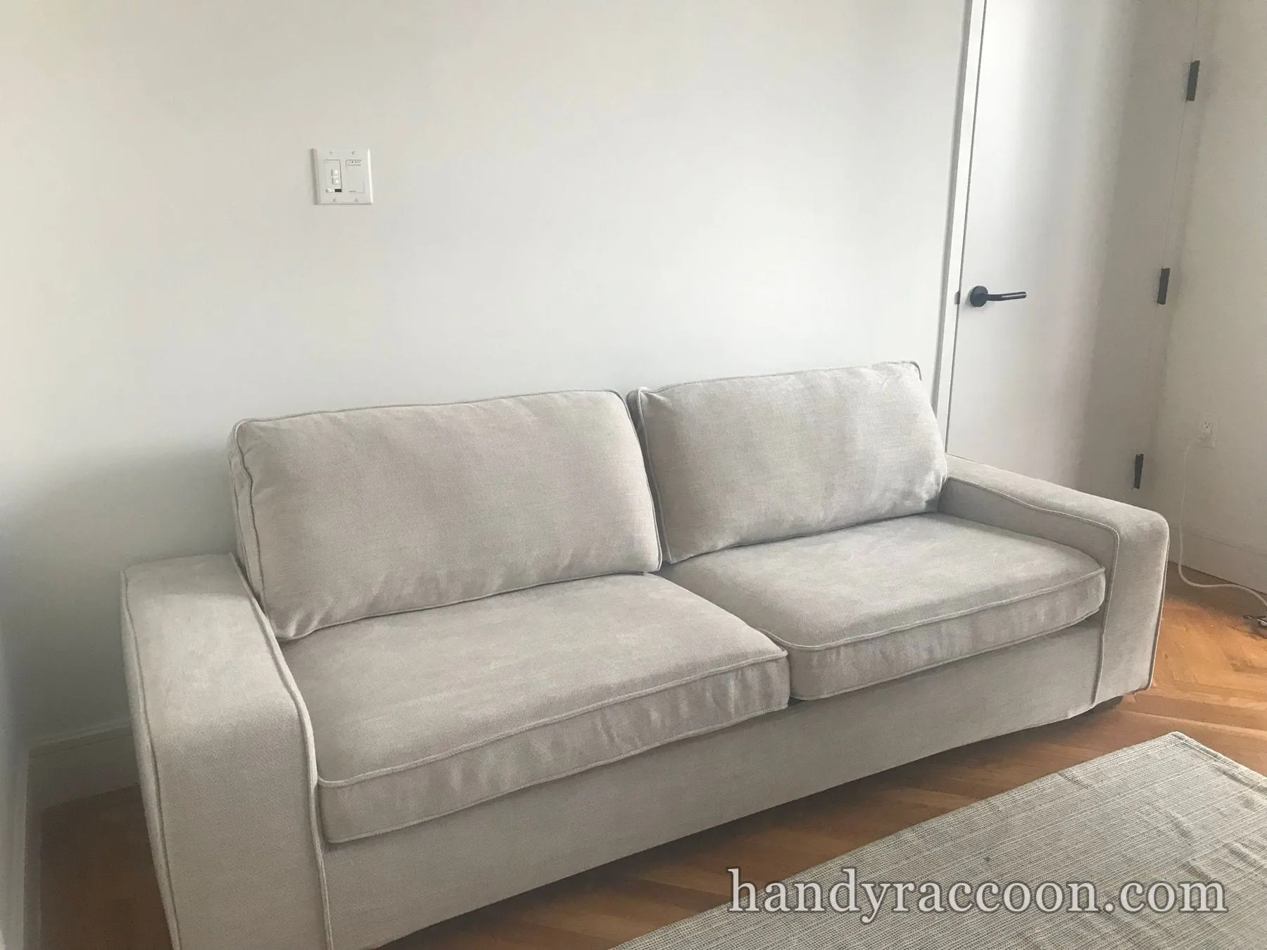Light grey two-cushion upholstered sofa placed against a white wall on a wood floor