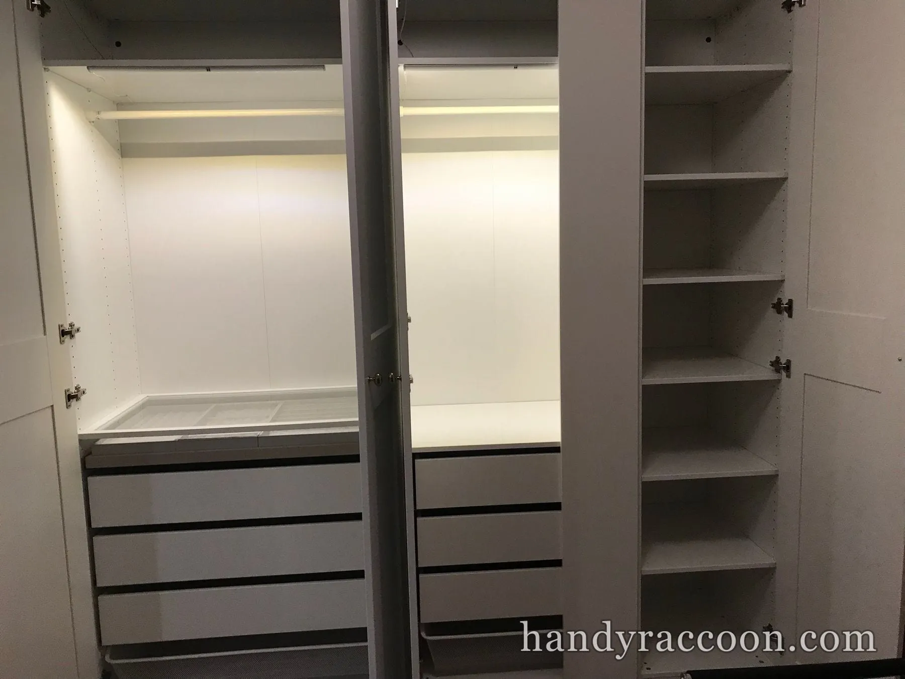 Open white wardrobe interior with stacked drawers, a hanging rail and side shelves lit by LEDs