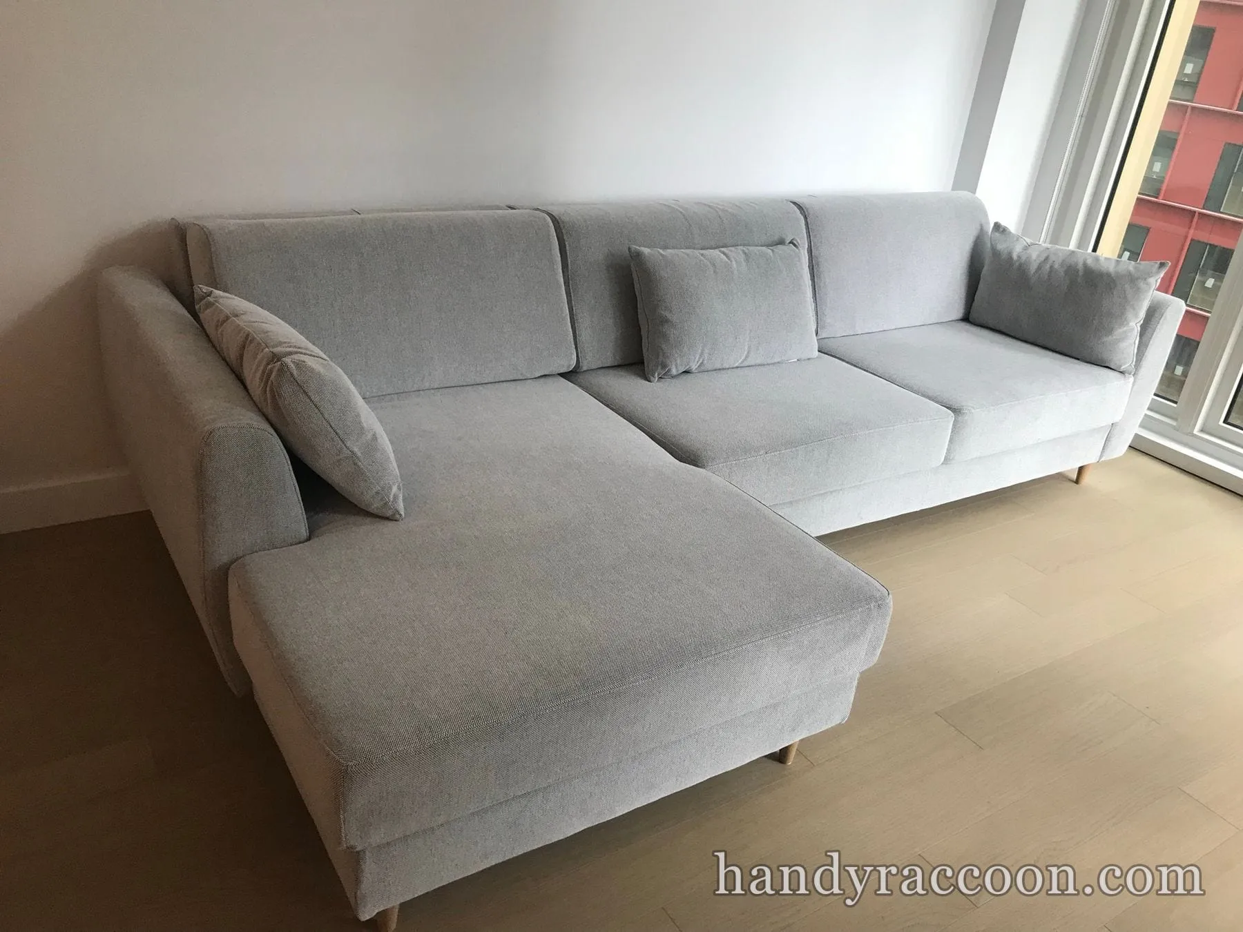 Light grey L-shaped sectional sofa with chaise and cushions in a bright living room by a window.
