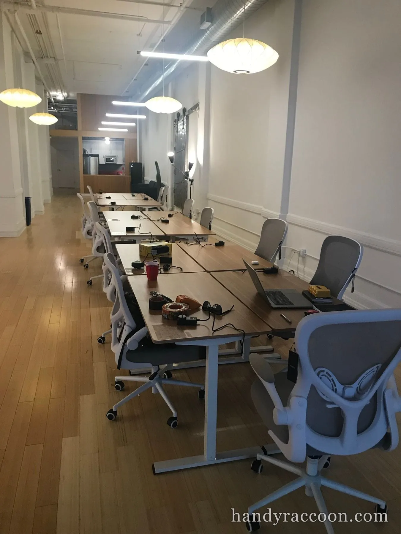 Row of wood standing desks and grey mesh office chairs assembled in an open loft workspace.