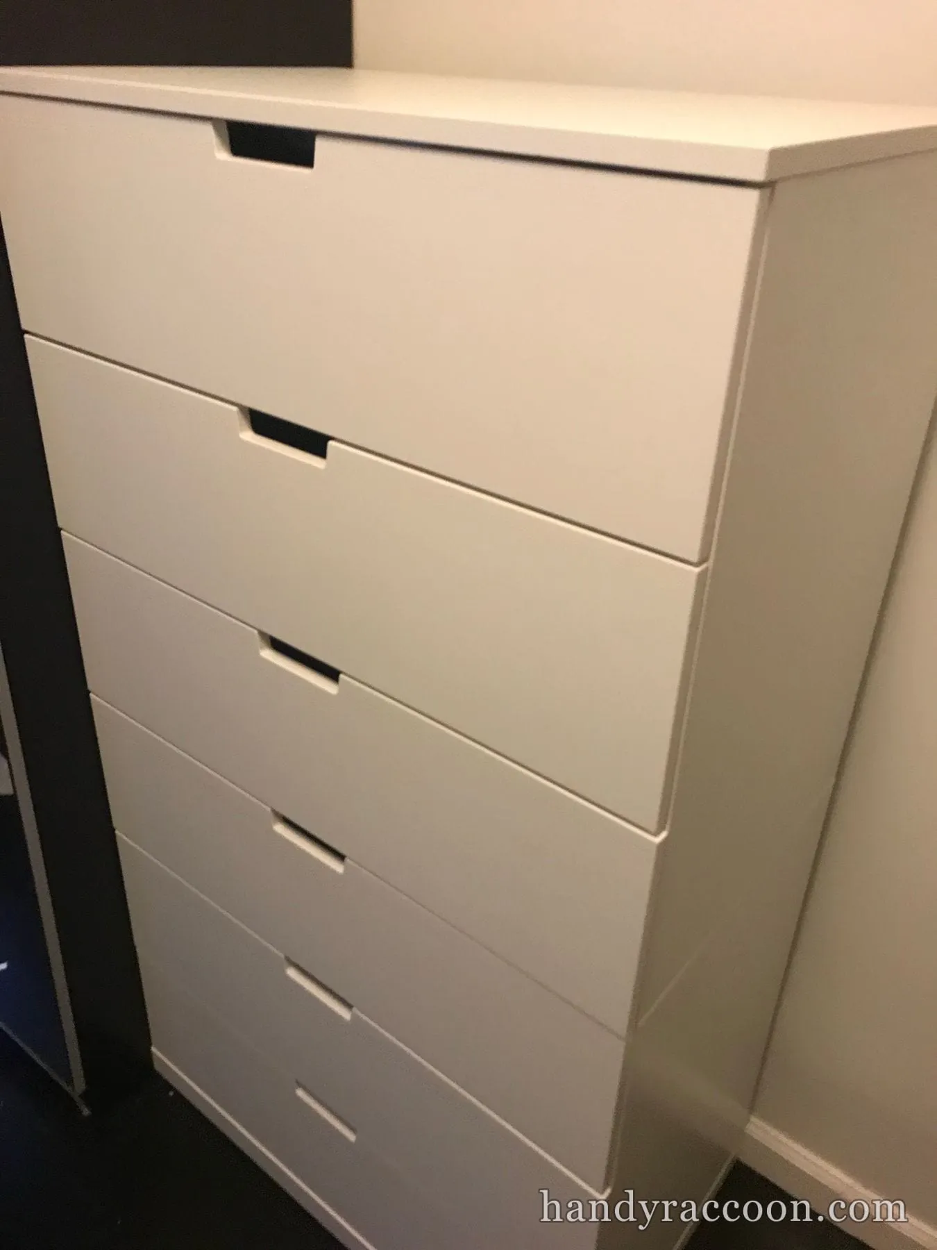 Tall white multi-drawer dresser assembled and standing against a dark wall.