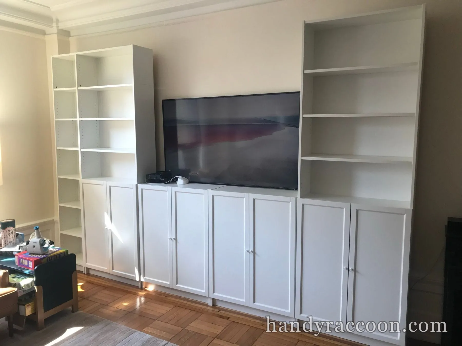 White floor-to-ceiling bookcases and lower cabinets flanking a large flat-screen TV in a living room.