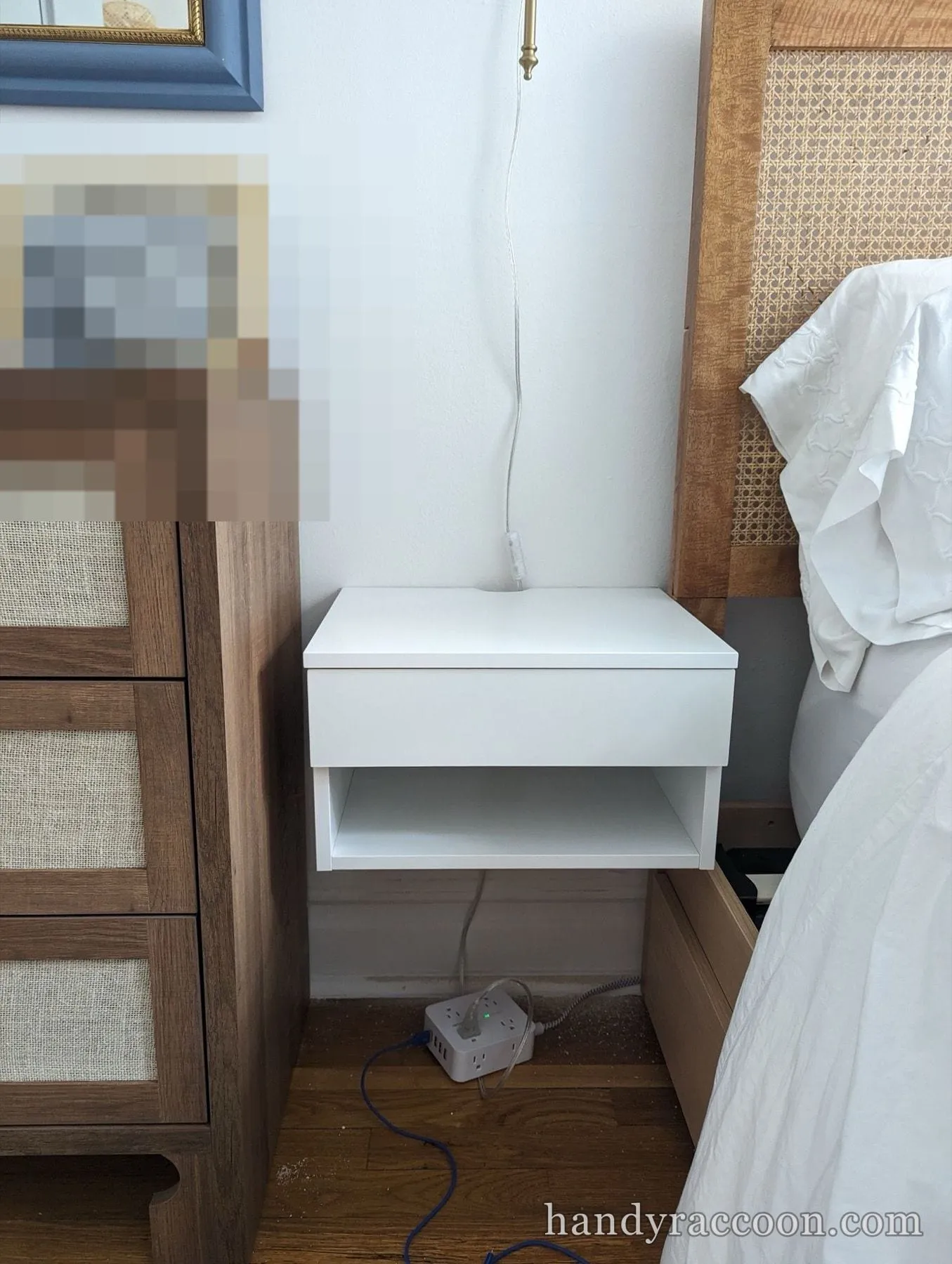 White floating nightstand with a drawer and open shelf mounted on the wall next to a caned headboard.