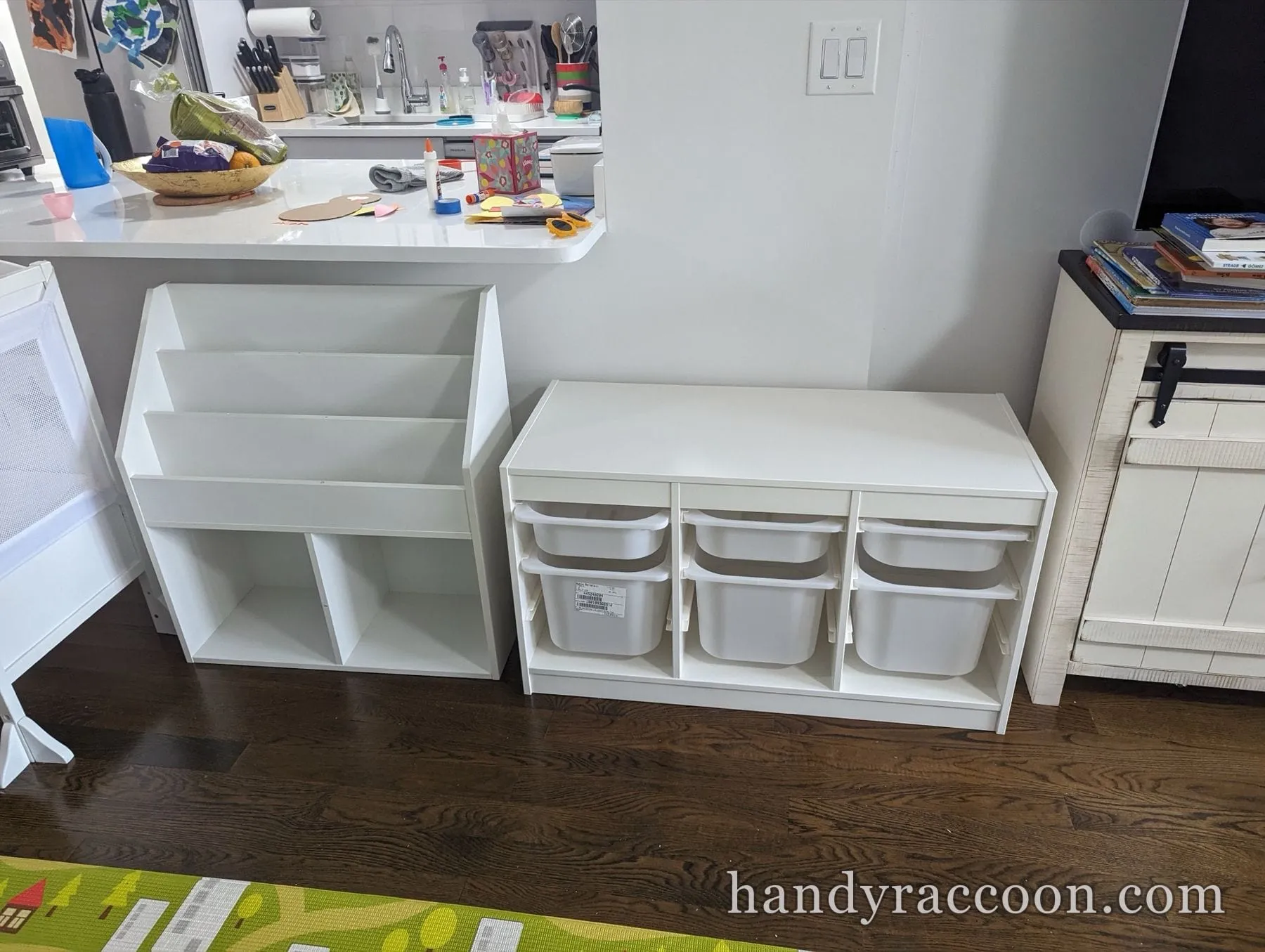 White kids' book display shelf and a three-bin white storage unit beside a kitchen counter.
