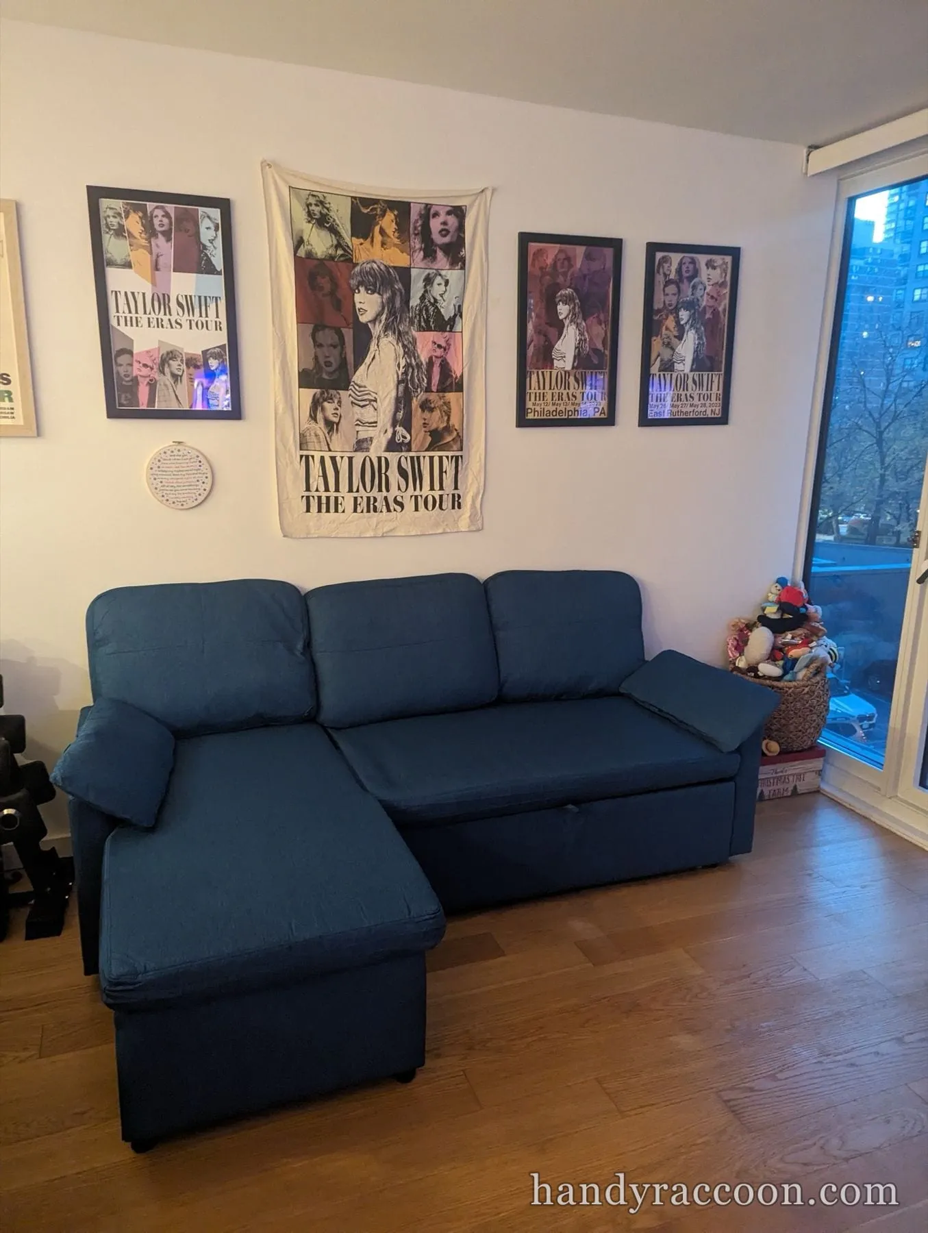 Blue fabric sectional sleeper sofa with a chaise against a poster-covered wall.