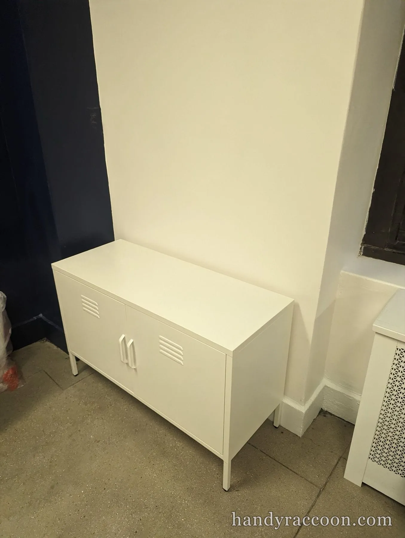 White metal two-door locker console with vents on a concrete floor by a navy wall.