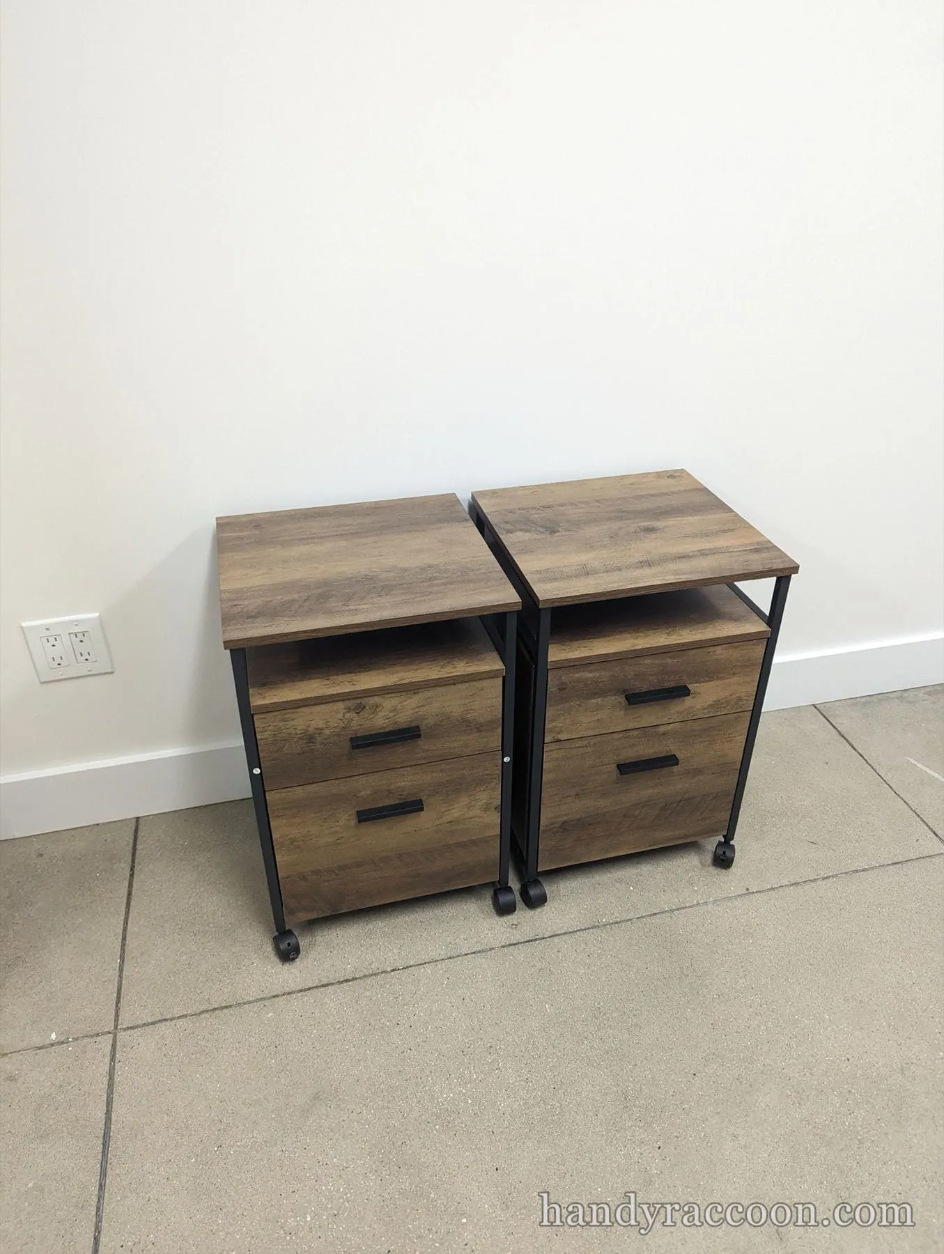 Two wood-grain and black metal two-drawer file cabinets on wheels against a white wall.