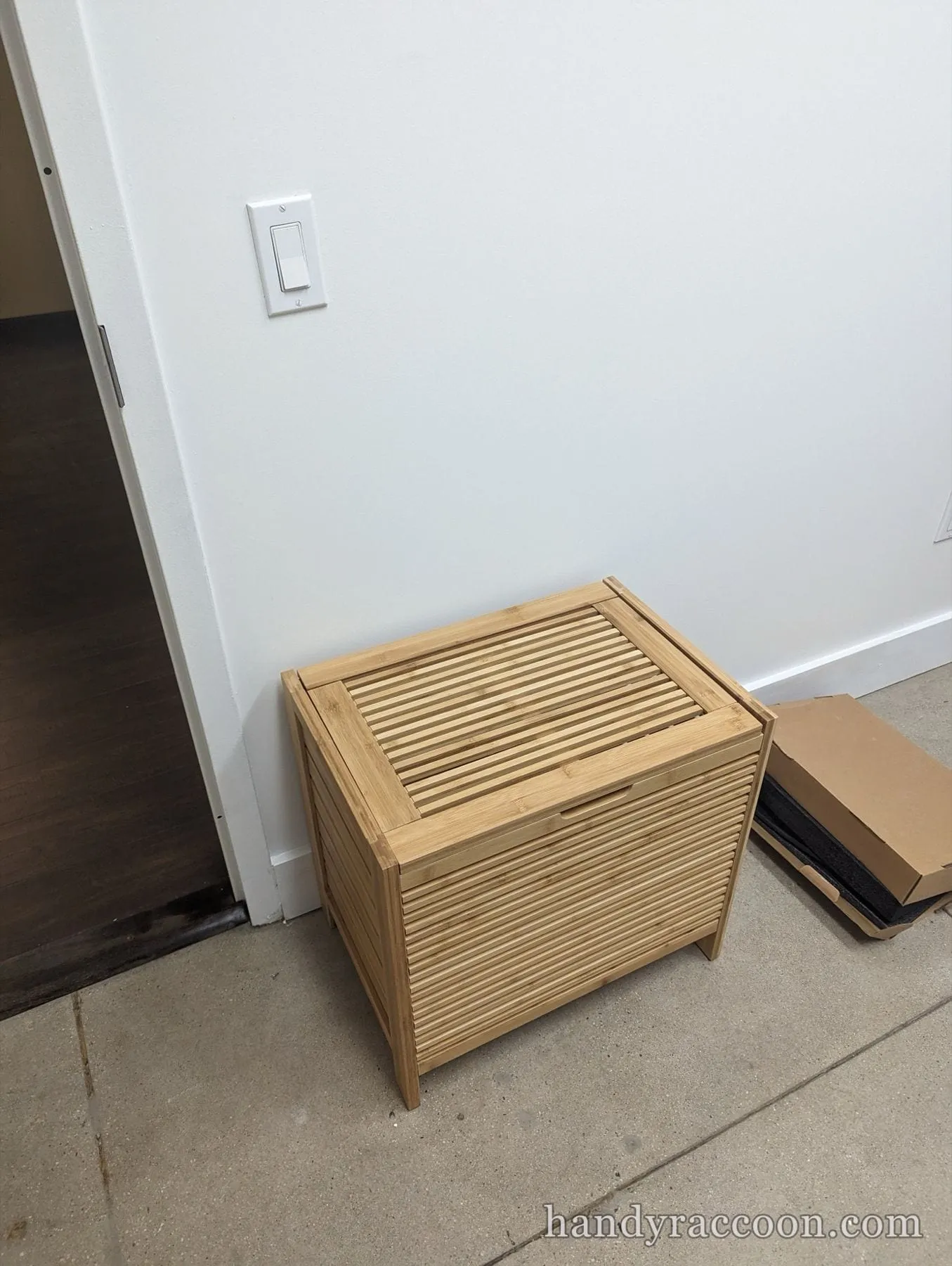 Bamboo slatted storage box with a lid on the floor beside a light switch.