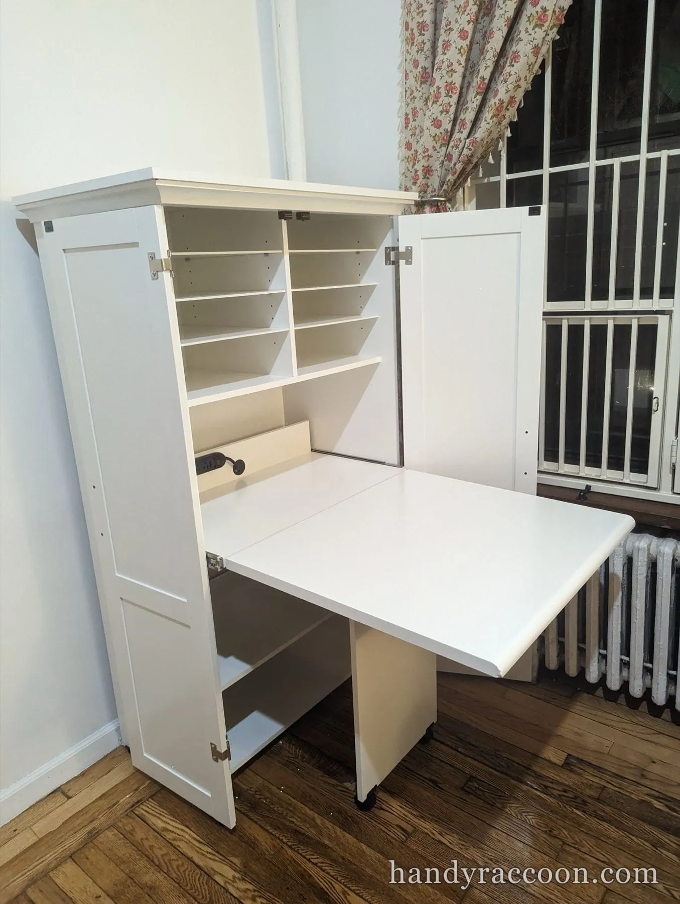 White cabinet open with a fold-out desk surface extended, interior shelving and a power strip above.