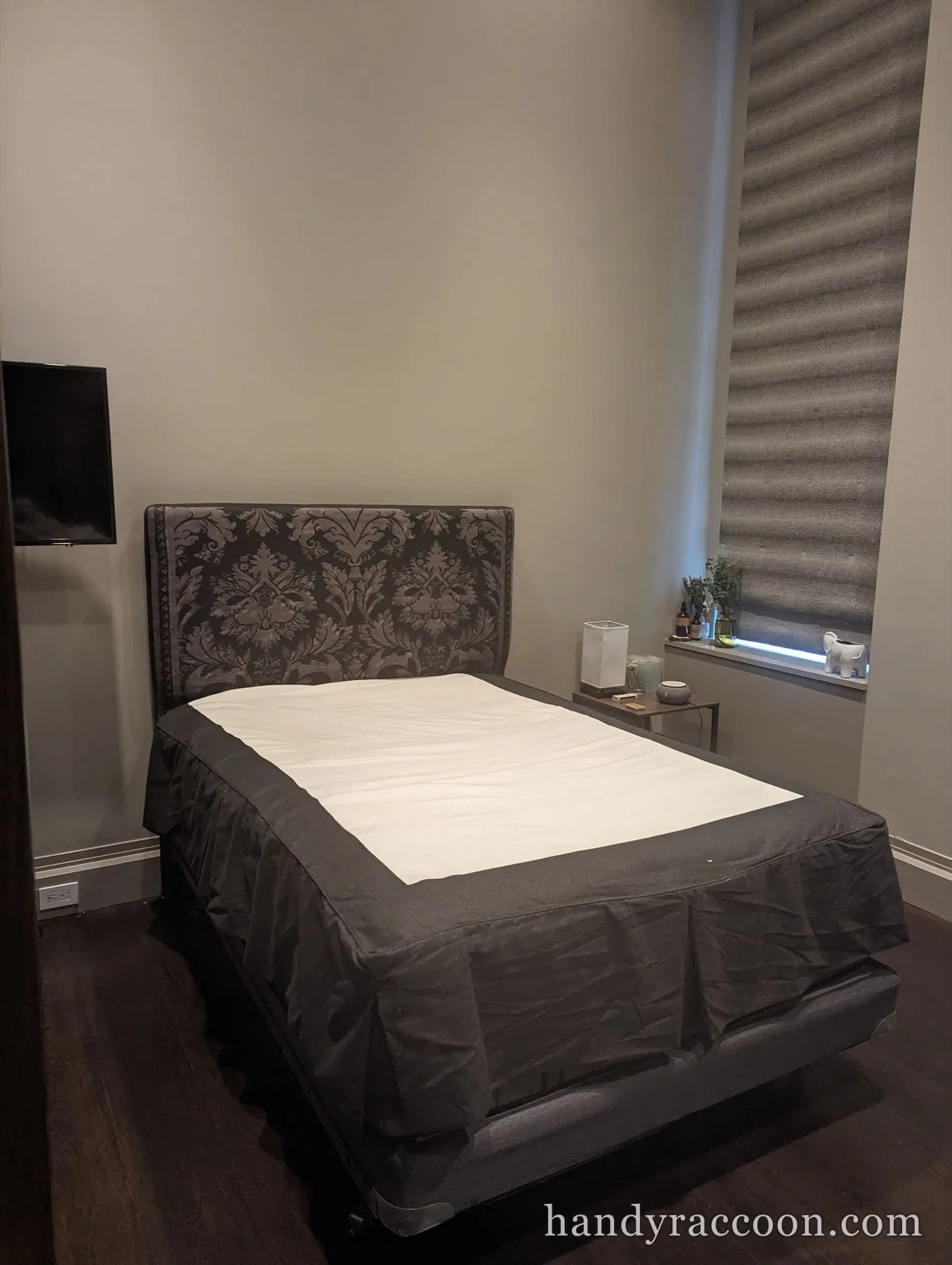 Gray upholstered bed with a damask patterned headboard made up in a dim bedroom.