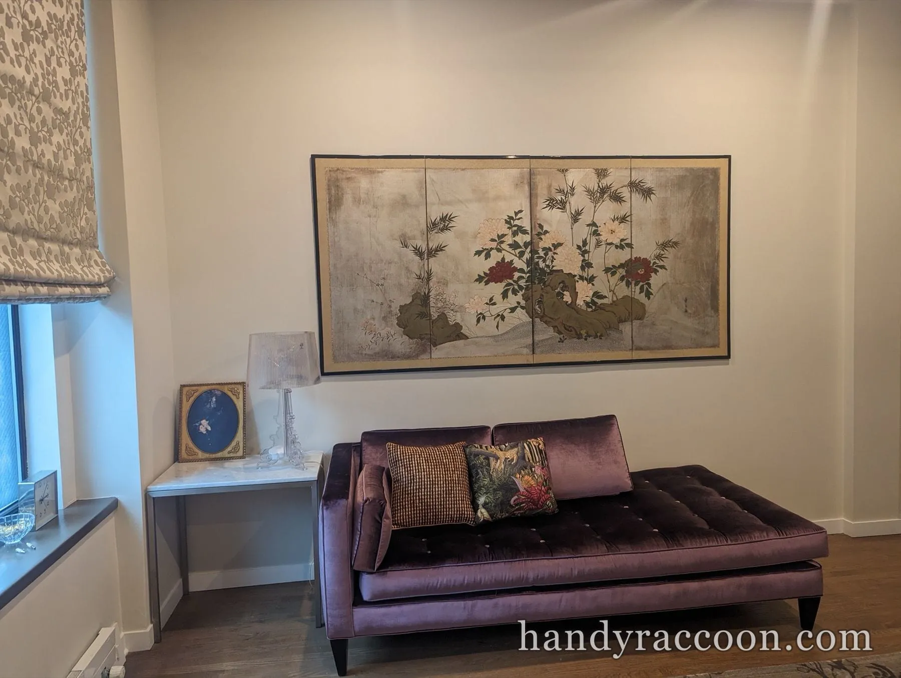 Purple velvet daybed with pillows below a large four-panel framed artwork on a beige wall.