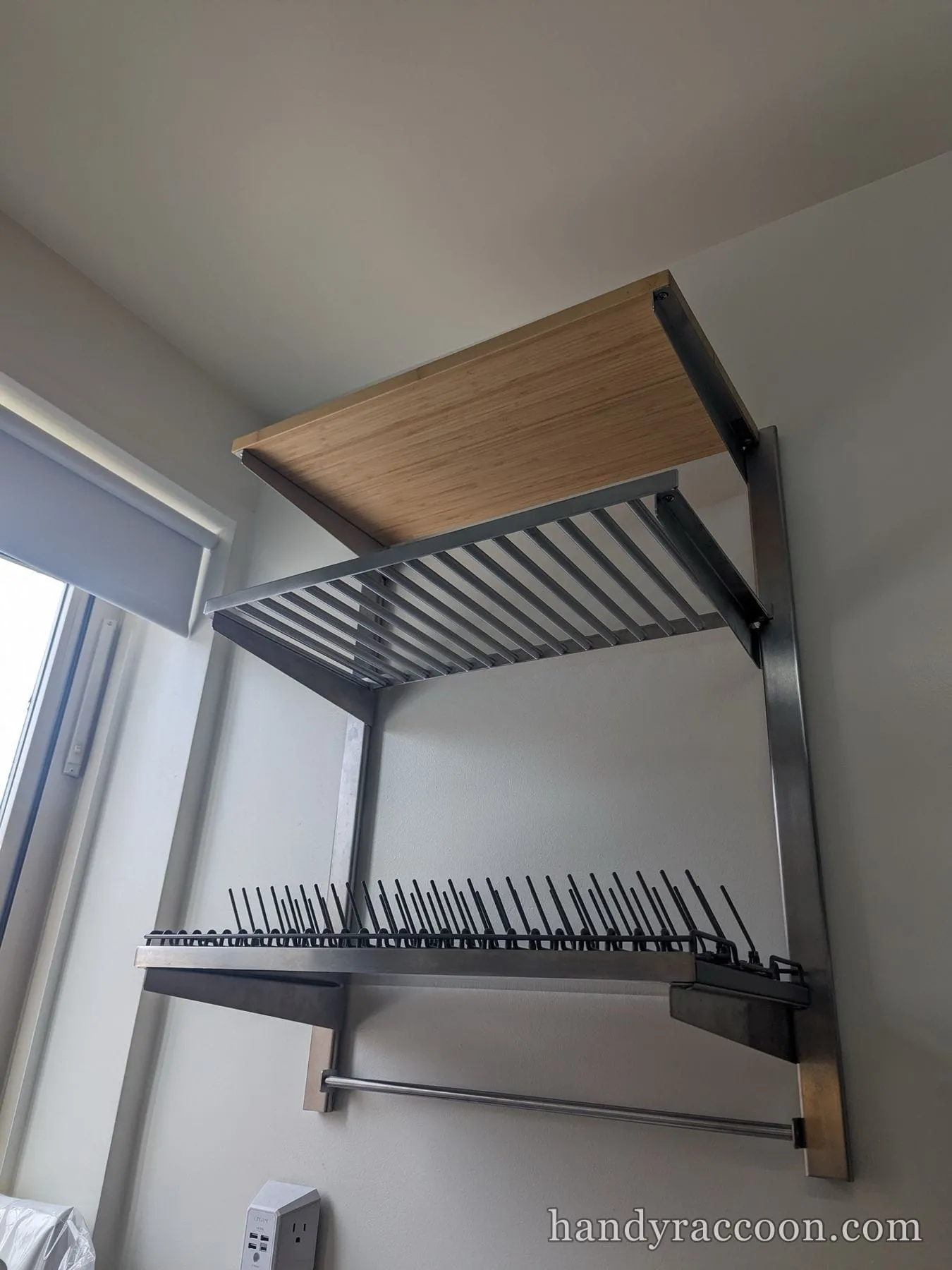 Wall-mounted stainless dish drying rack with a bamboo shelf installed above a counter.