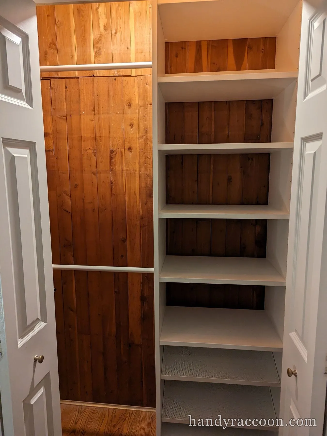 Reach-in closet with white shelves installed on the right and wood plank paneling with a hanging rod.