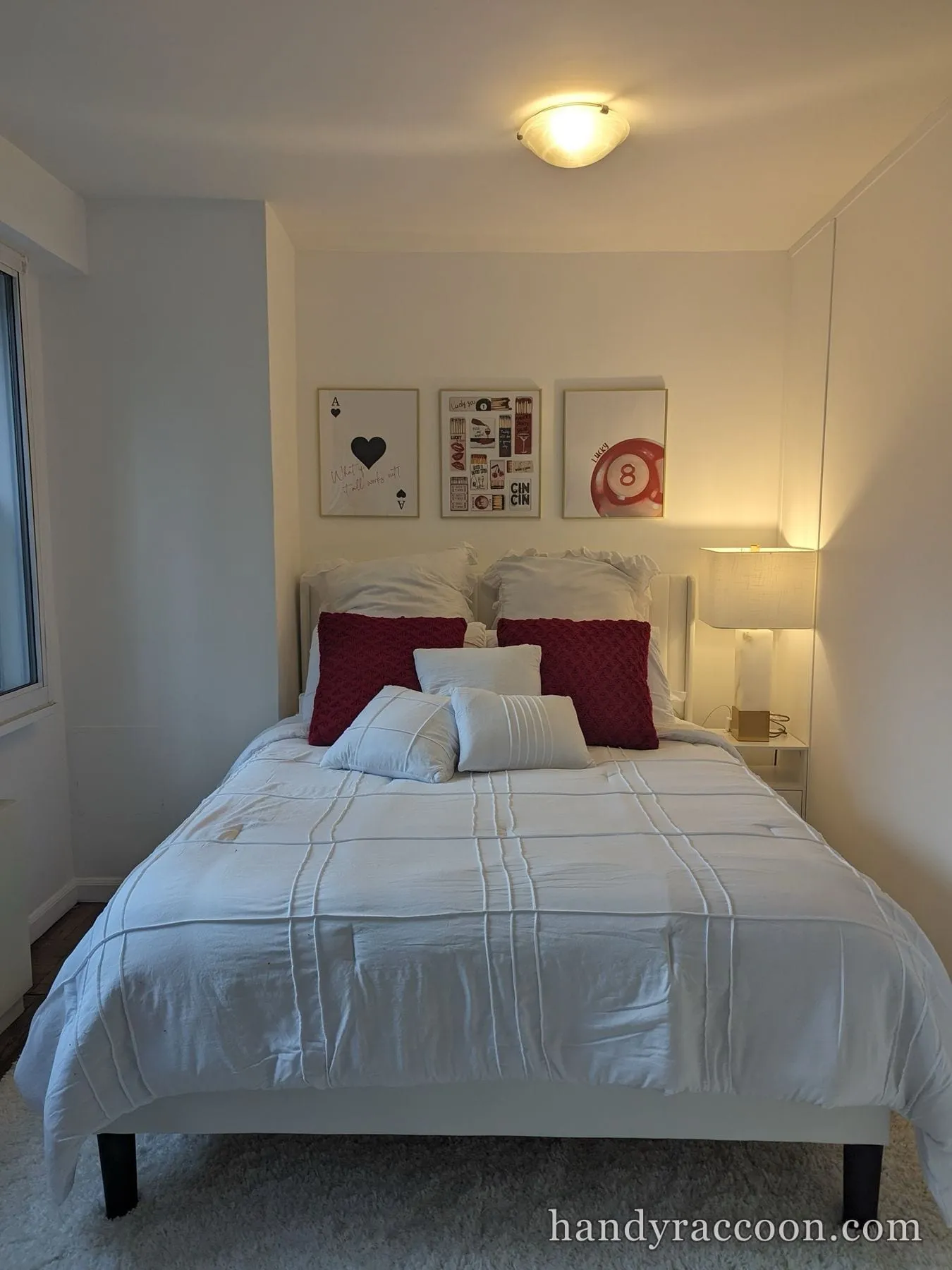 White upholstered bed with white bedding and red accent pillows under three framed prints.