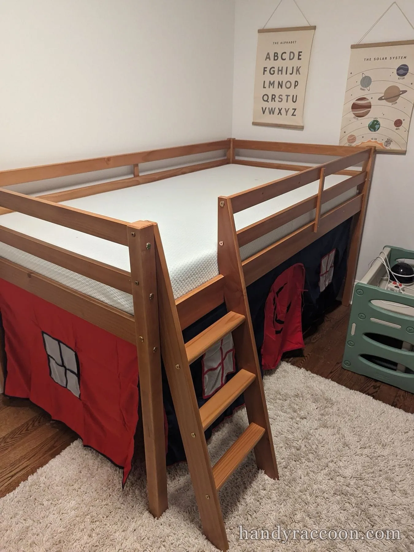 Wooden junior loft bed with a ladder, white mattress and a red and blue play tent underneath.