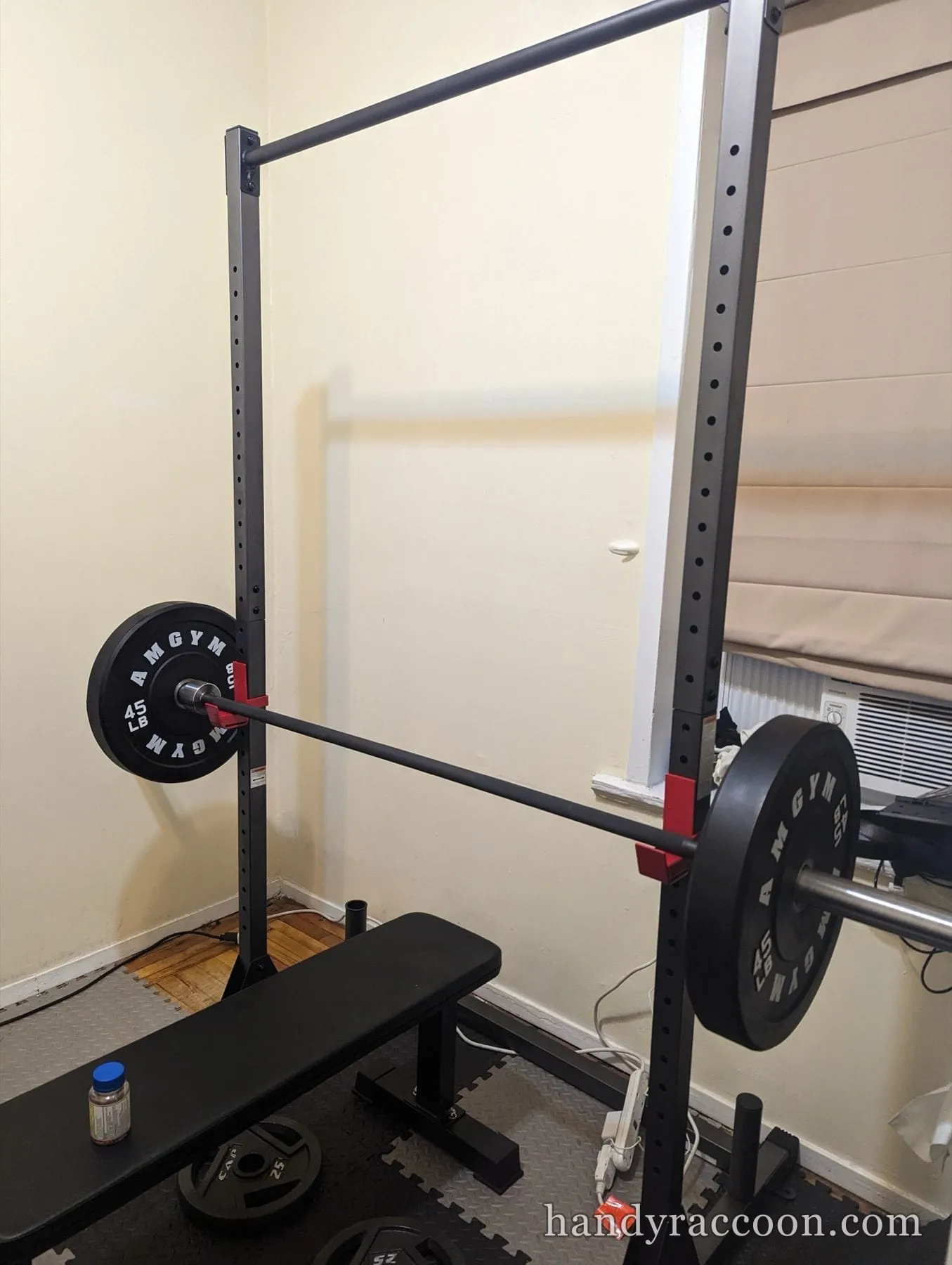 Steel squat rack holding a barbell with bumper plates next to a padded flat bench.