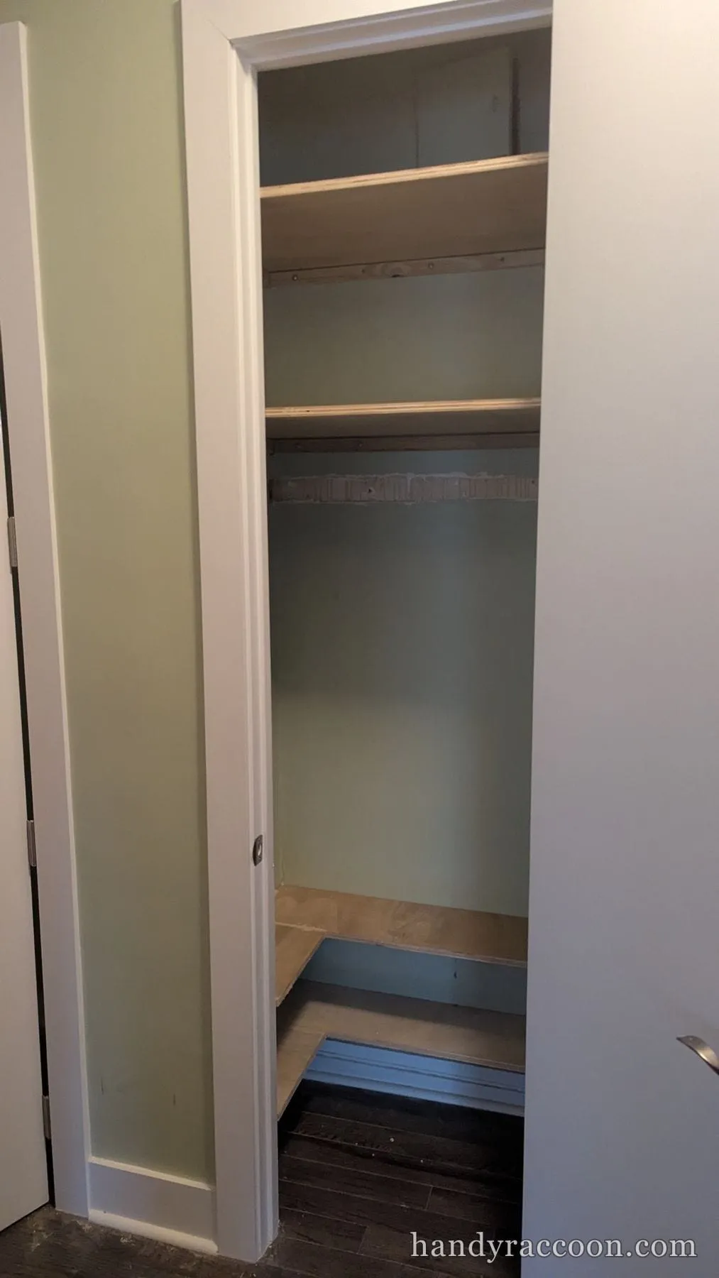 Closet with two installed plywood shelves and a sage green interior, sliding door open.