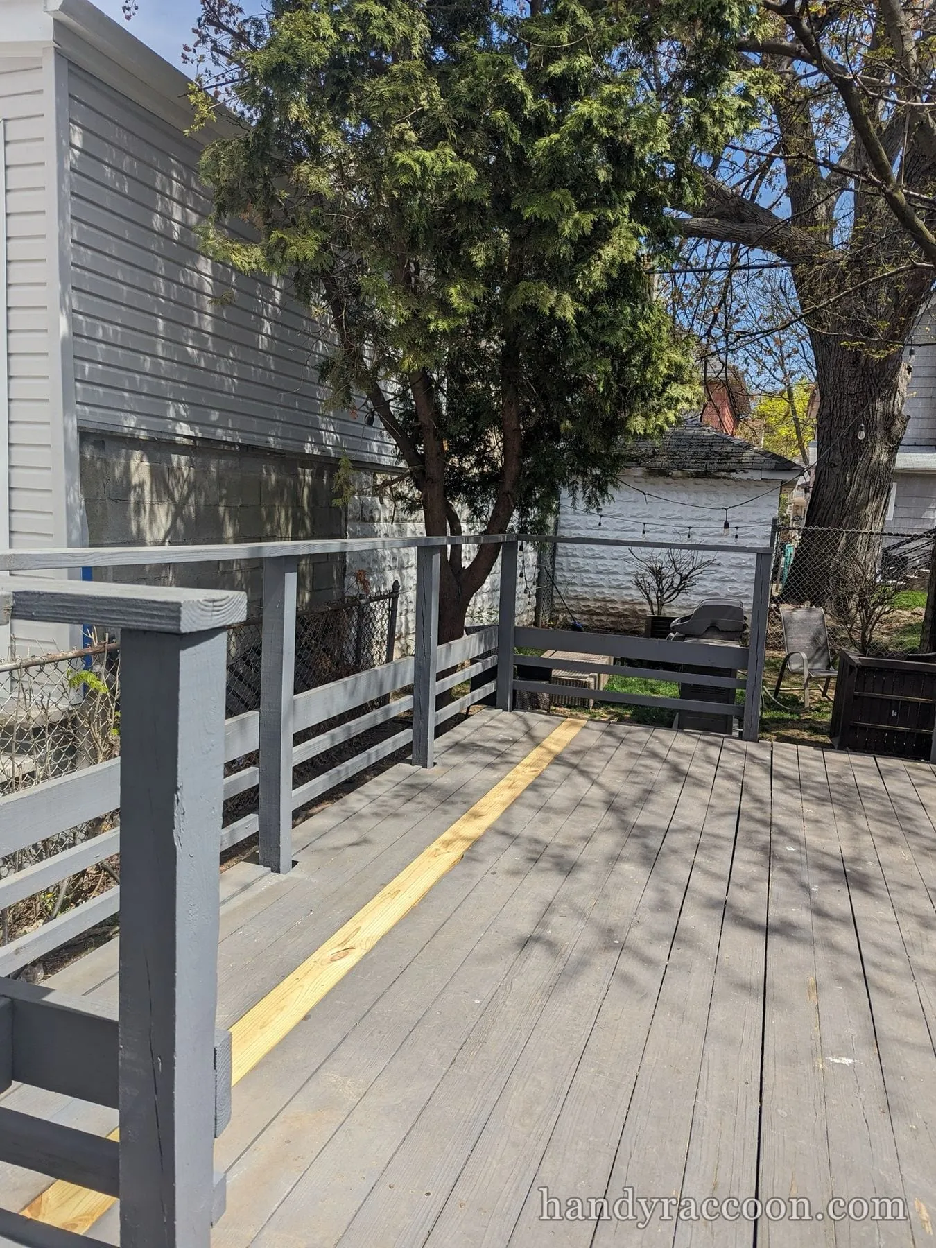 Gray backyard deck with railings and one fresh light board installed near the rail.