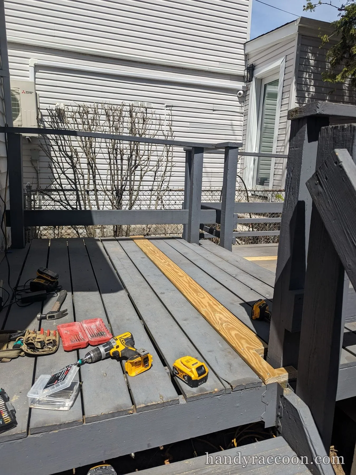 Gray deck mid-repair with a new board and cordless drills and drill bits spread out.