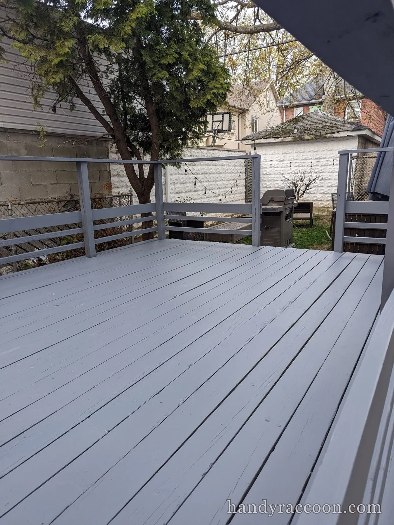 Freshly painted light gray deck with gray railings looking out to a backyard and grill.
