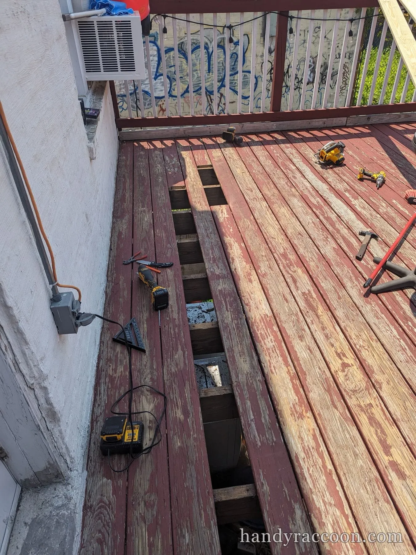 Maroon deck with several boards removed exposing the joists, tools scattered around.
