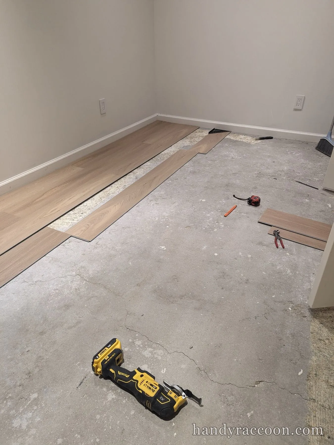 Room mid-installation with plank flooring starting along the wall over concrete, tools on the floor.