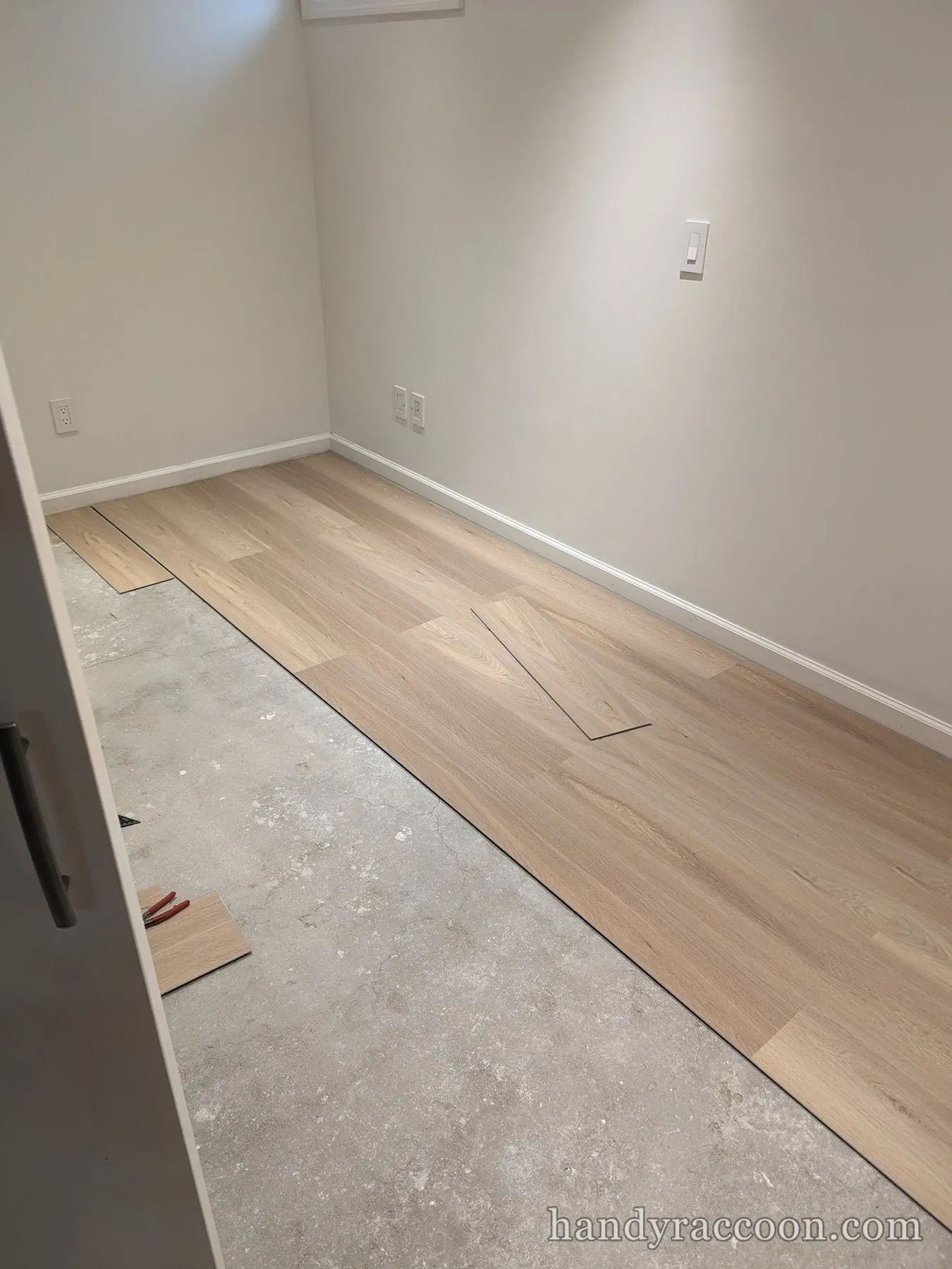 Light wood-look plank flooring partly installed over a concrete subfloor along a wall.