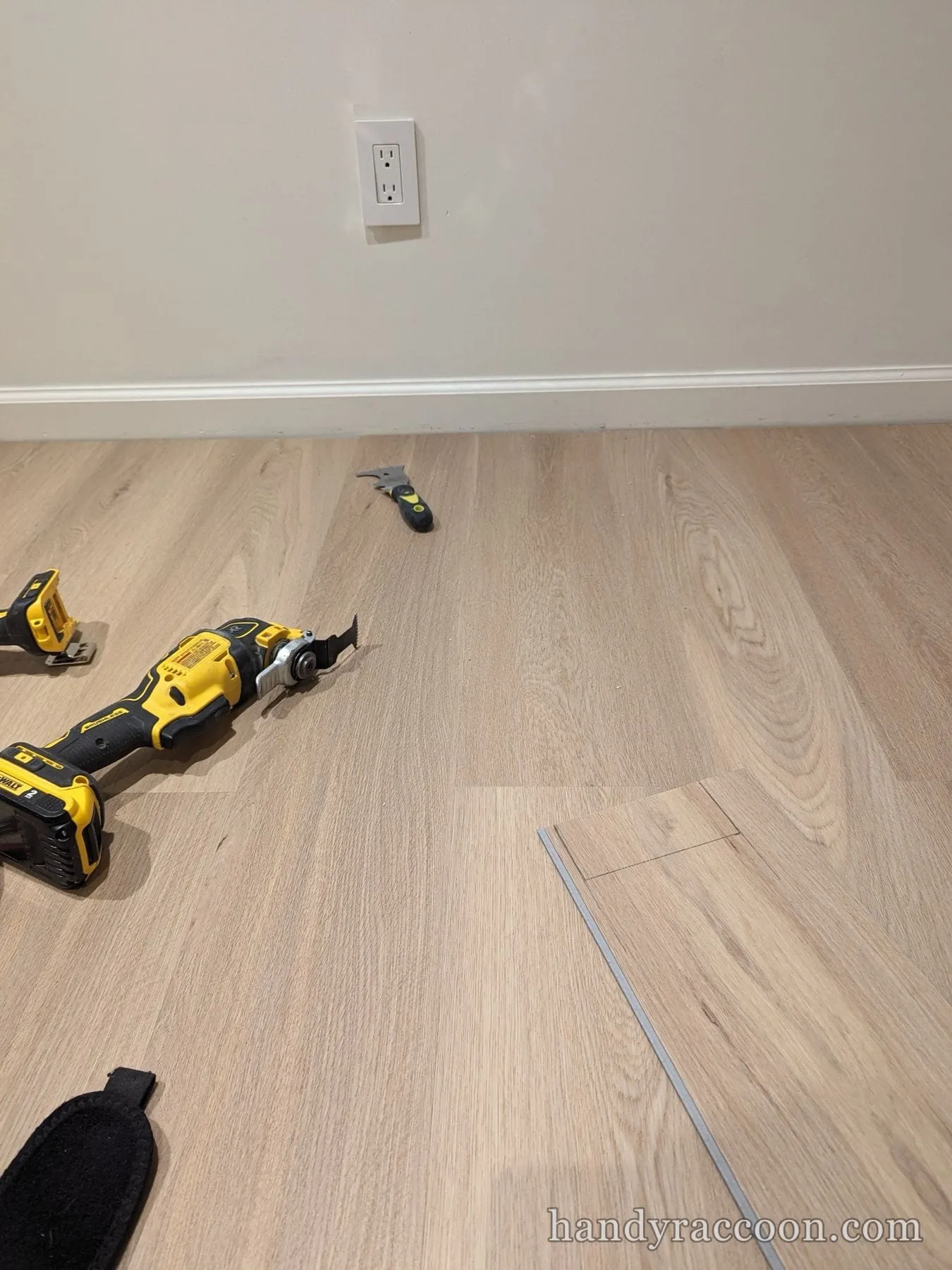 Close-up of installed light plank flooring with a power tool and utility knife resting on it.