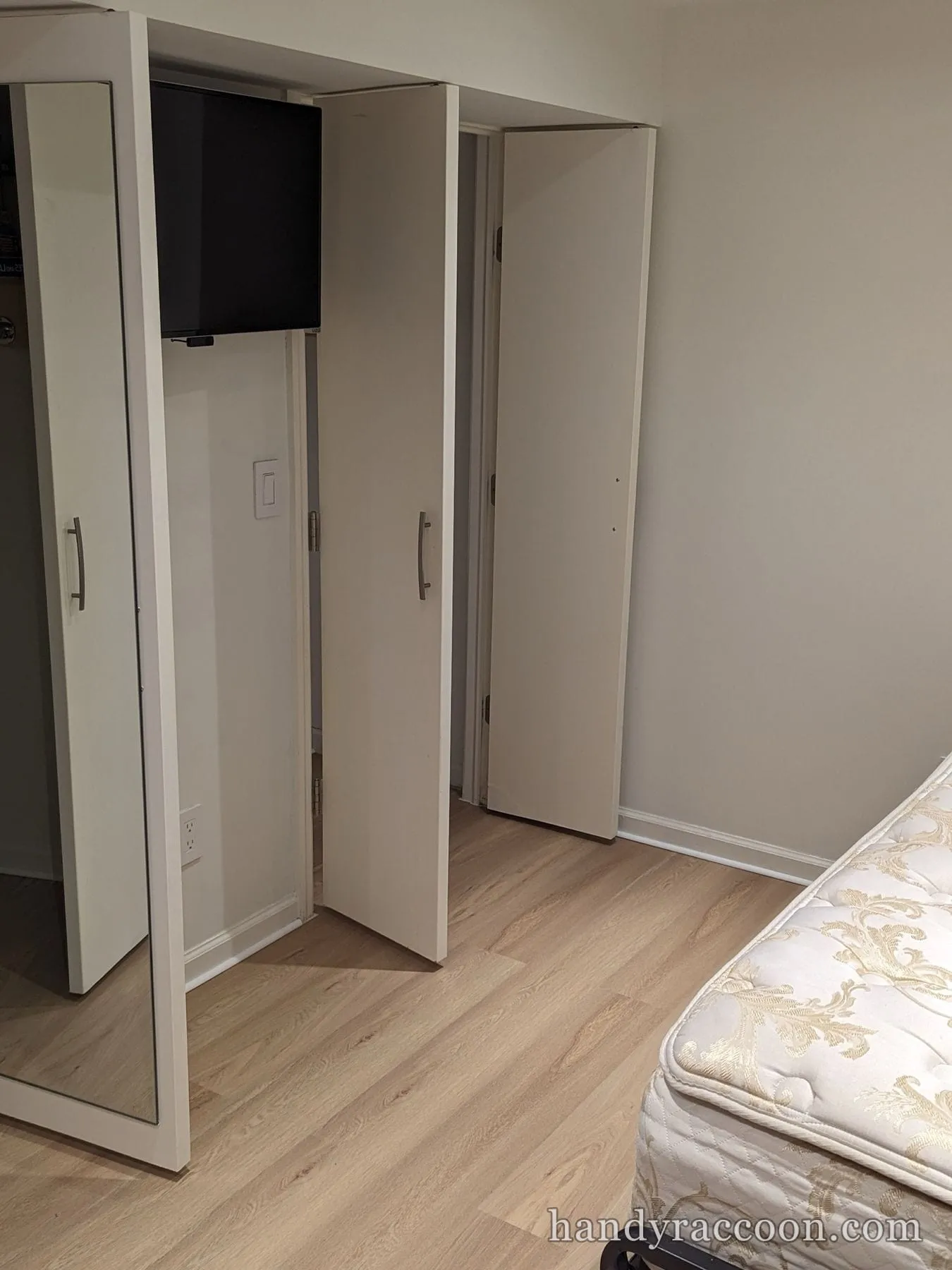 Finished light wood-look plank floor in a bedroom with white mirrored closet doors and a mounted TV.