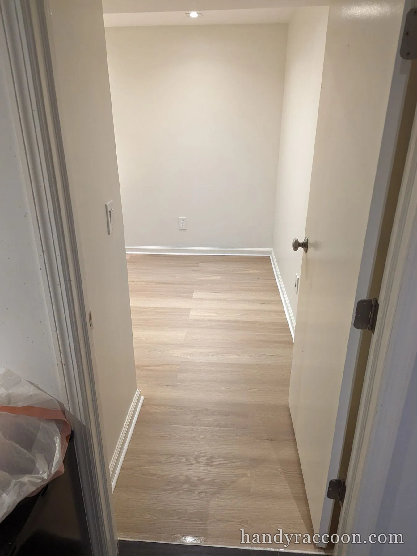 Finished light plank flooring in a small room seen through an open doorway.