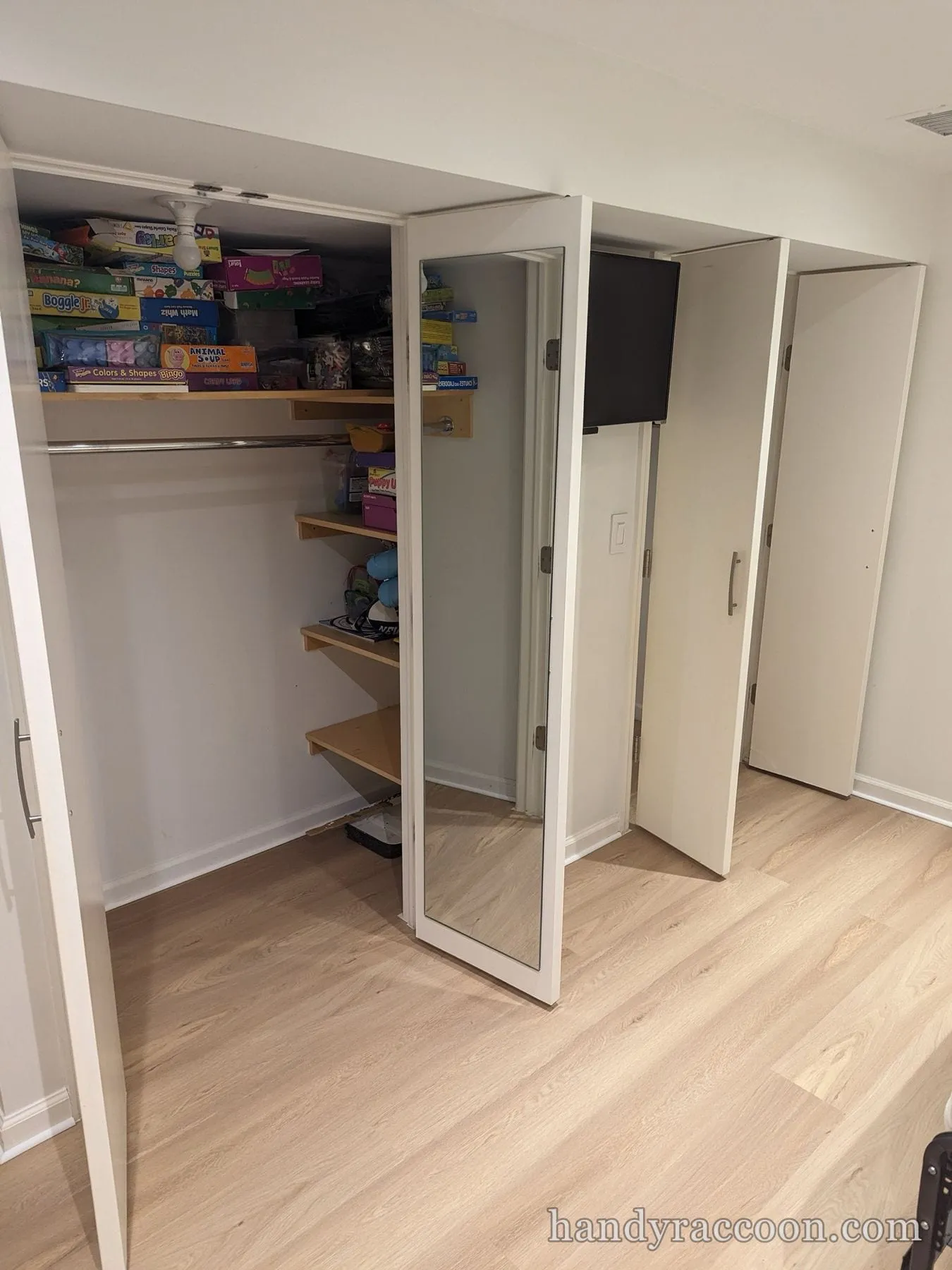 Light plank flooring in front of an open closet with shelves of boxed games and a mounted TV.