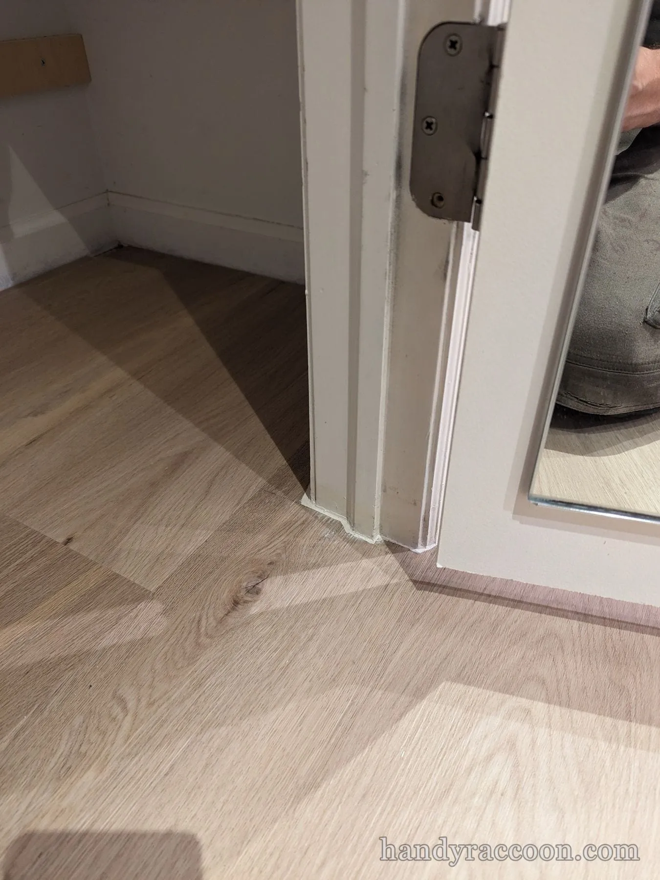 Close-up of light plank flooring fitted cleanly against a white door casing with a hinge.
