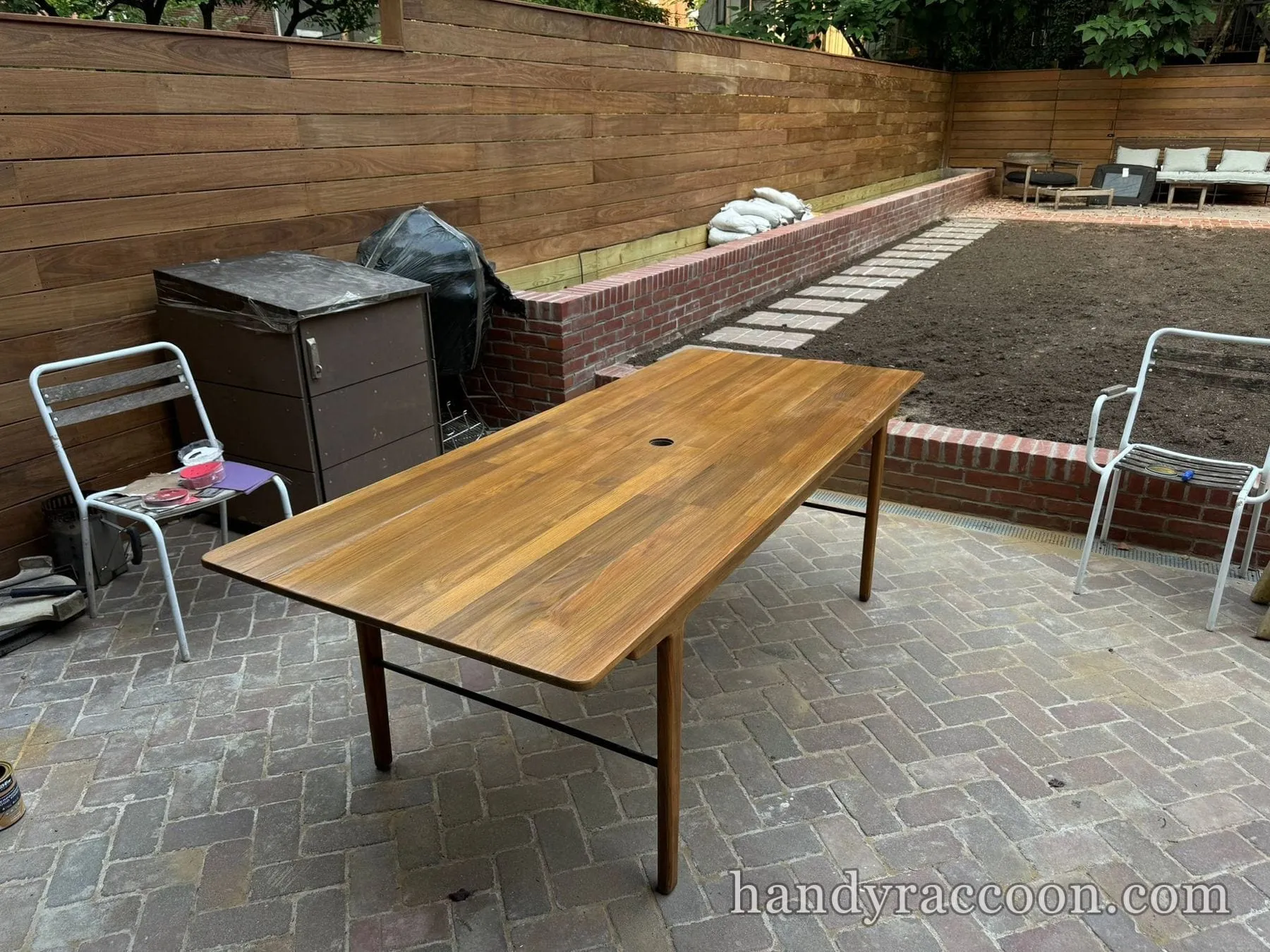 Rectangular wood patio table with fresh warm finish on a brick paver patio by a wood fence.
