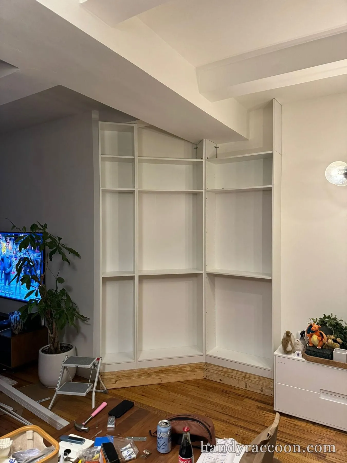 Empty white floor-to-ceiling corner bookcase built into a living room corner with a sloped ceiling.