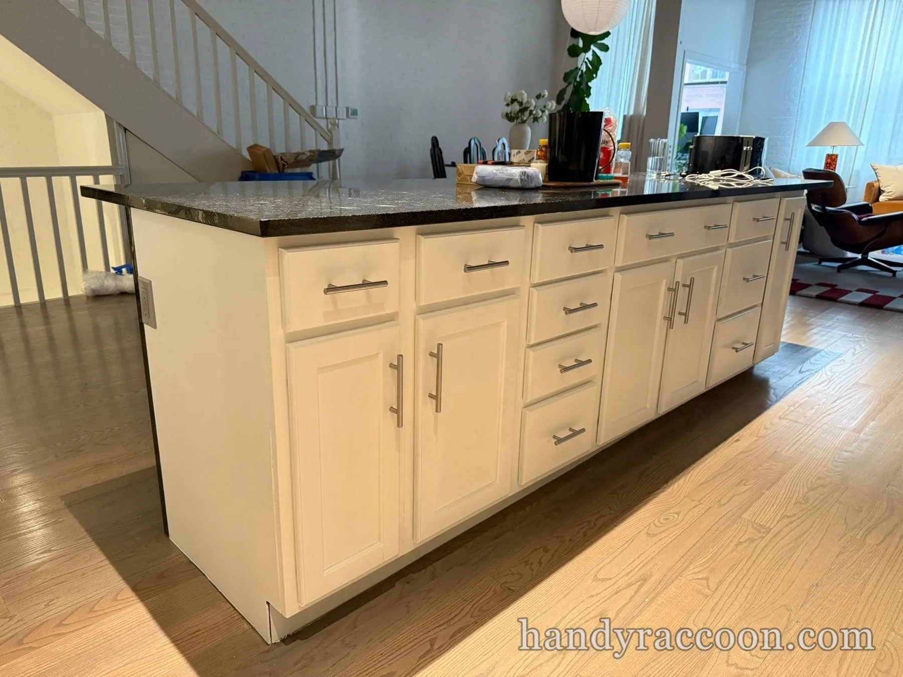 Long white kitchen island with paneled cabinets and dark granite countertop on a wood floor.