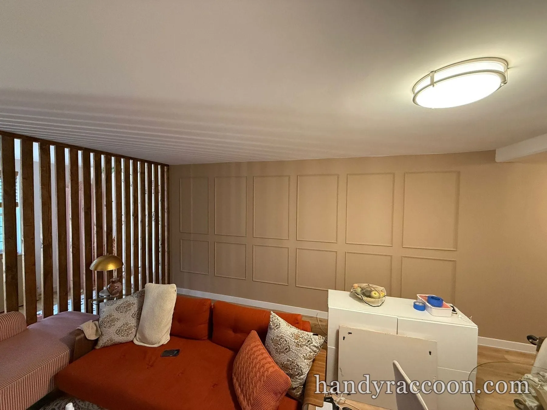 Living room with a vertical wood slat divider on the left and a beige grid-paneled accent wall.