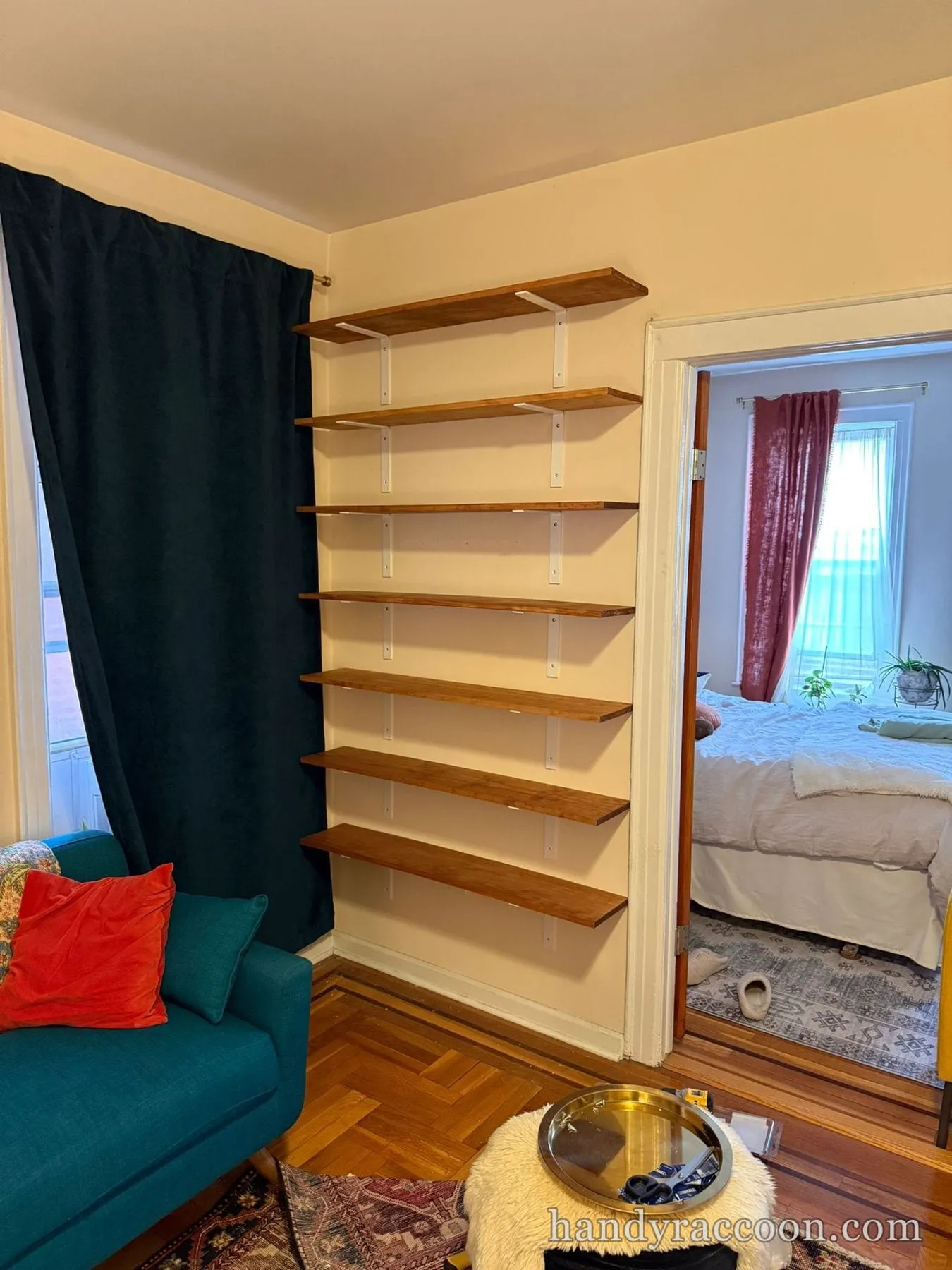 Seven stained wood shelves on white wall brackets installed beside a doorway to a bedroom.