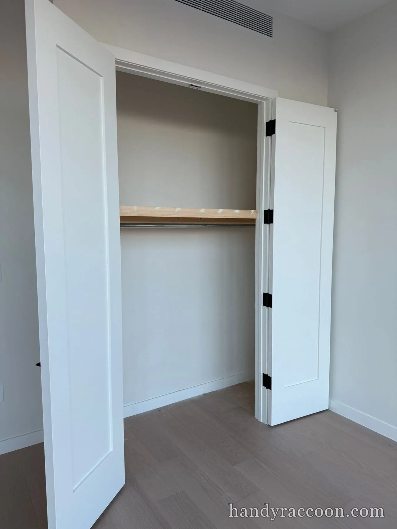 Open white bifold closet doors revealing a newly installed wood shelf and closet rod, empty.