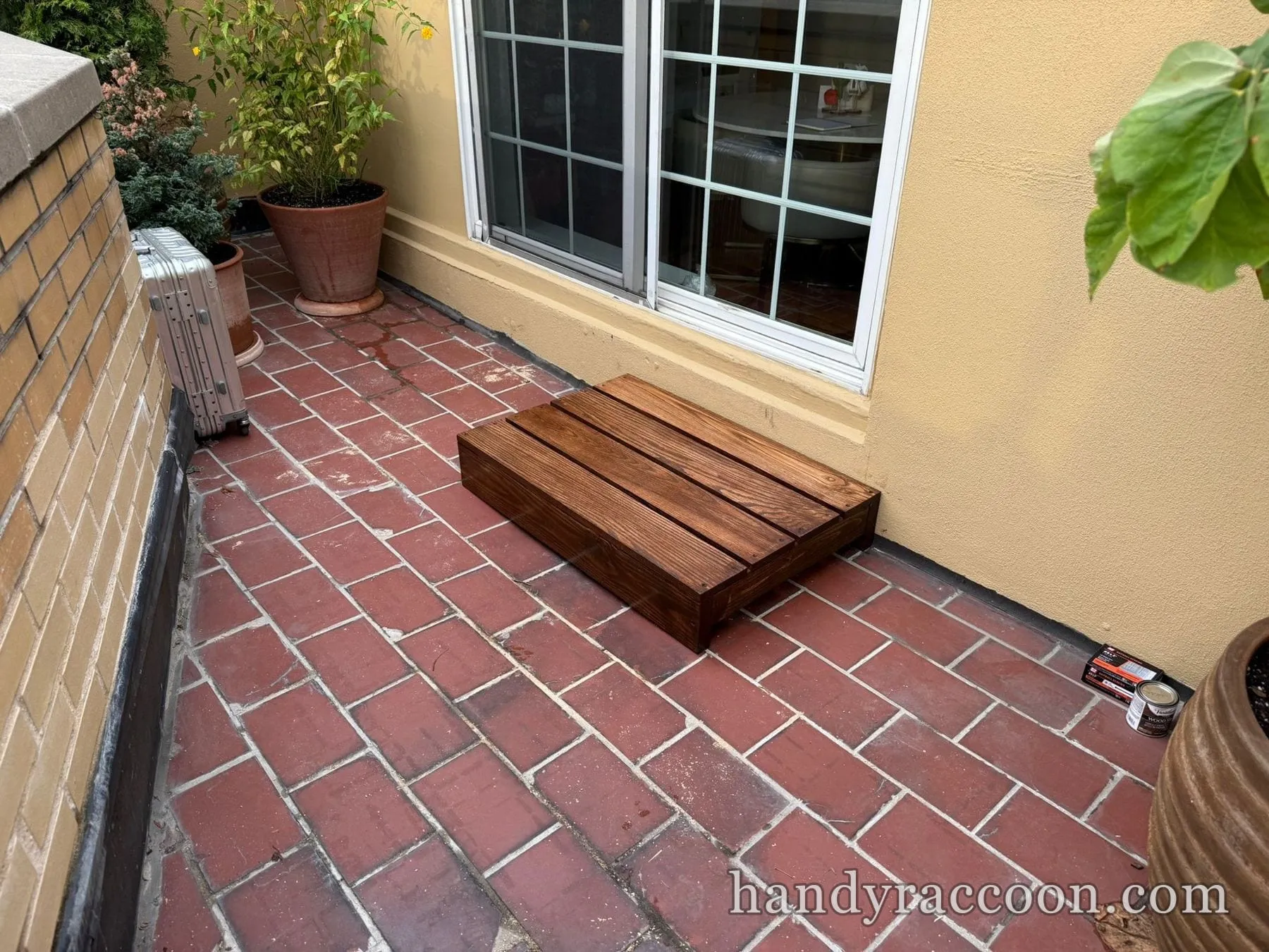 Low dark-stained wooden slat platform step on a red brick patio next to a sliding door.
