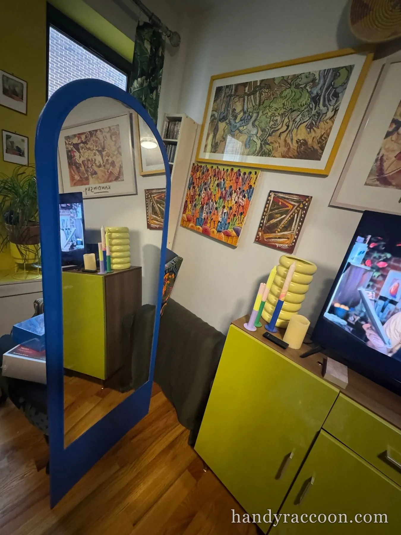 Tall blue arched wooden mirror frame standing in a colorful room hung with framed art prints.
