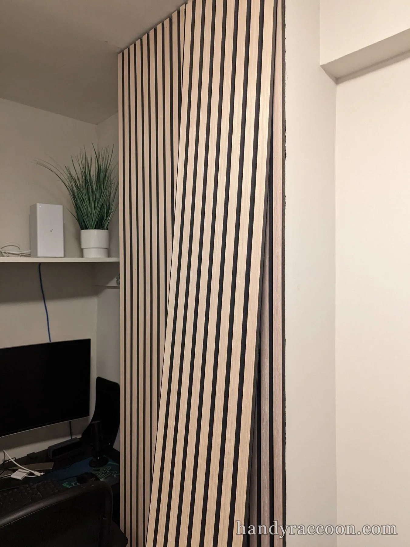 Vertical wood slat acoustic wall panels mounted in the corner of a home office beside a desk.