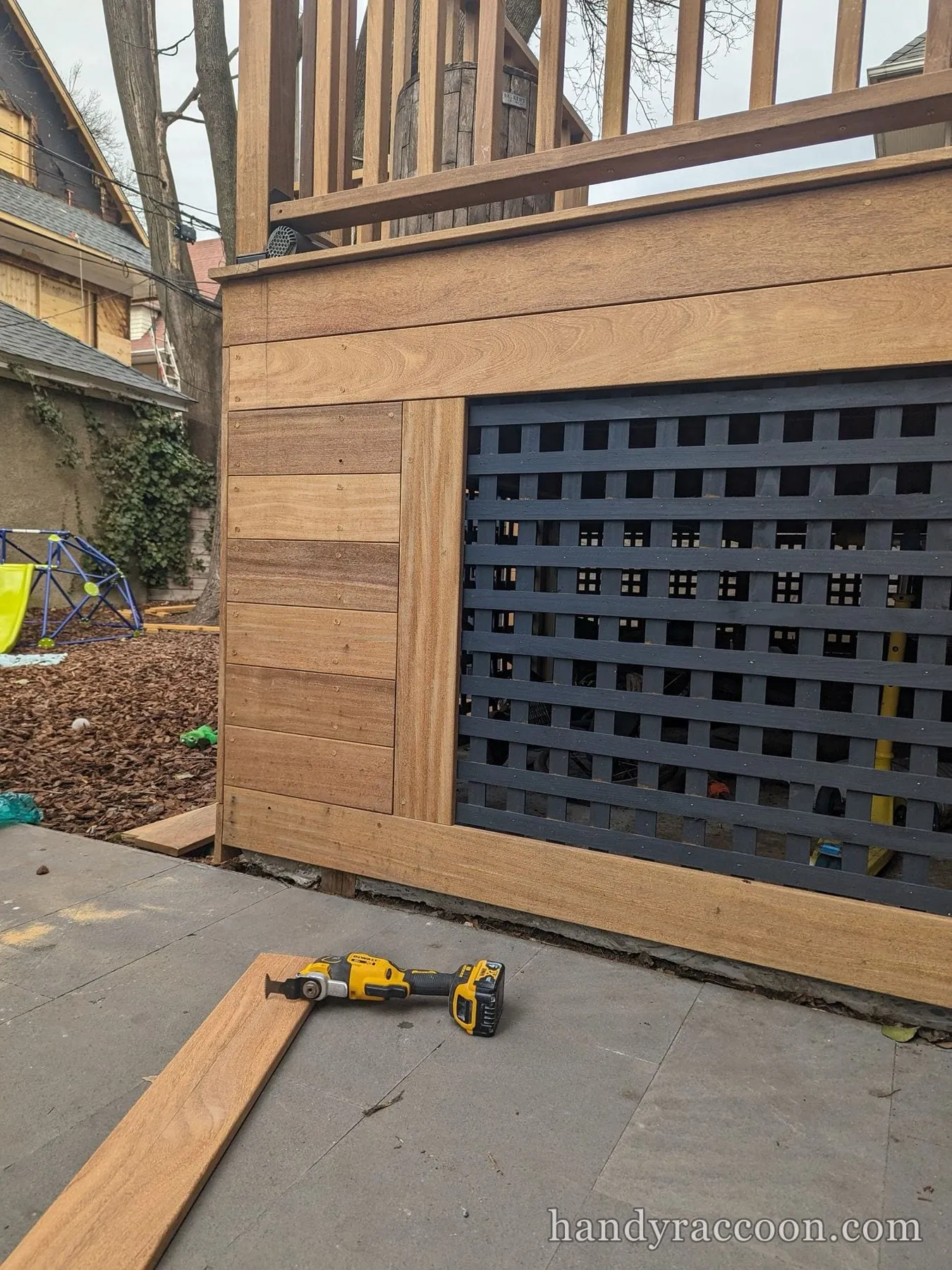 Finished hardwood deck skirting beside a dark blue lattice panel under a wood railing in a backyard.