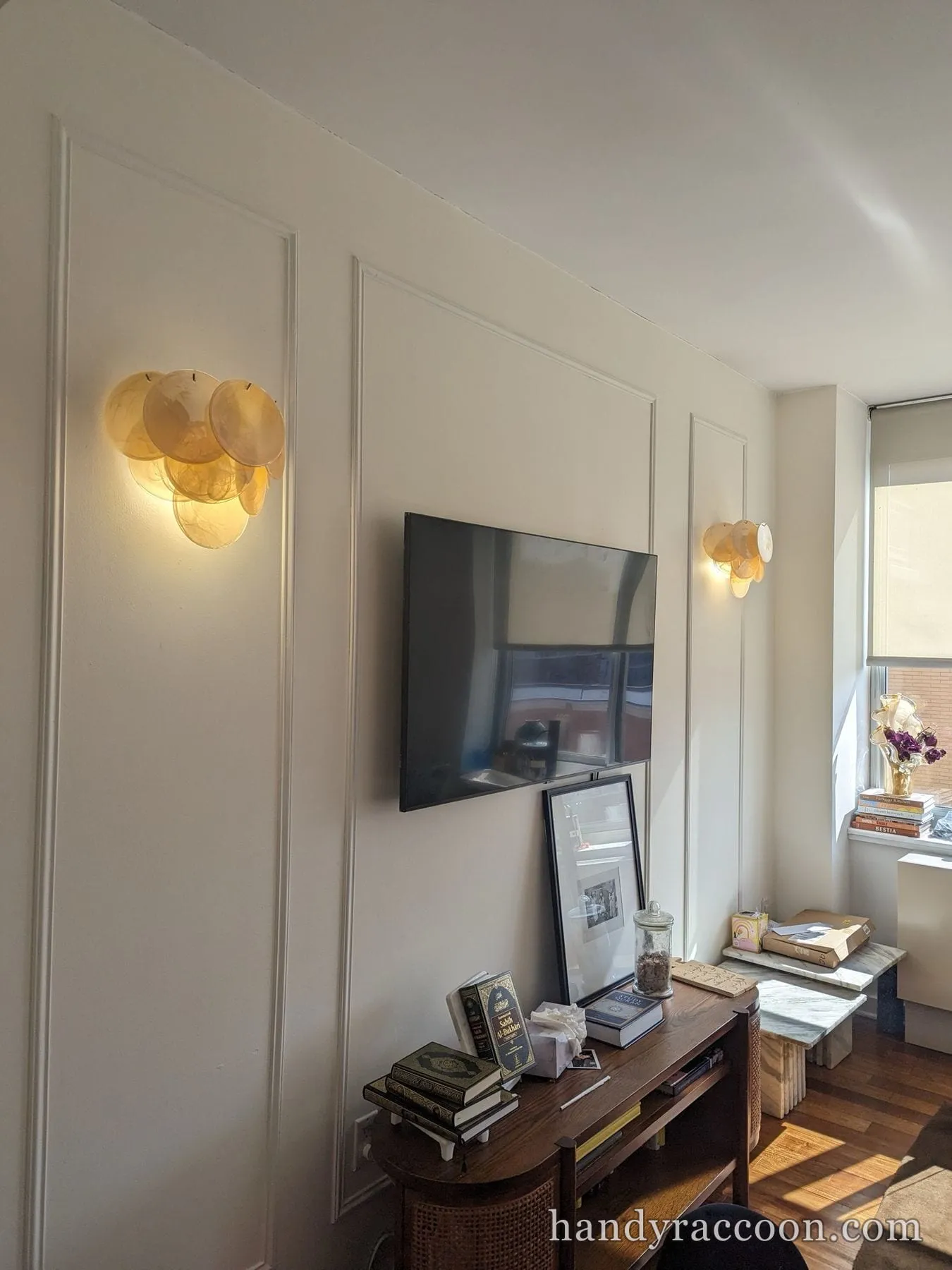 Finished white picture-frame wall paneling around a wall-mounted TV flanked by two lit sconces.