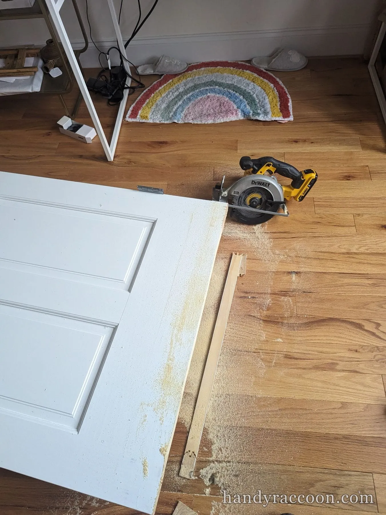 A white panel door lying on a wood floor being cut down with a yellow cordless circular saw.