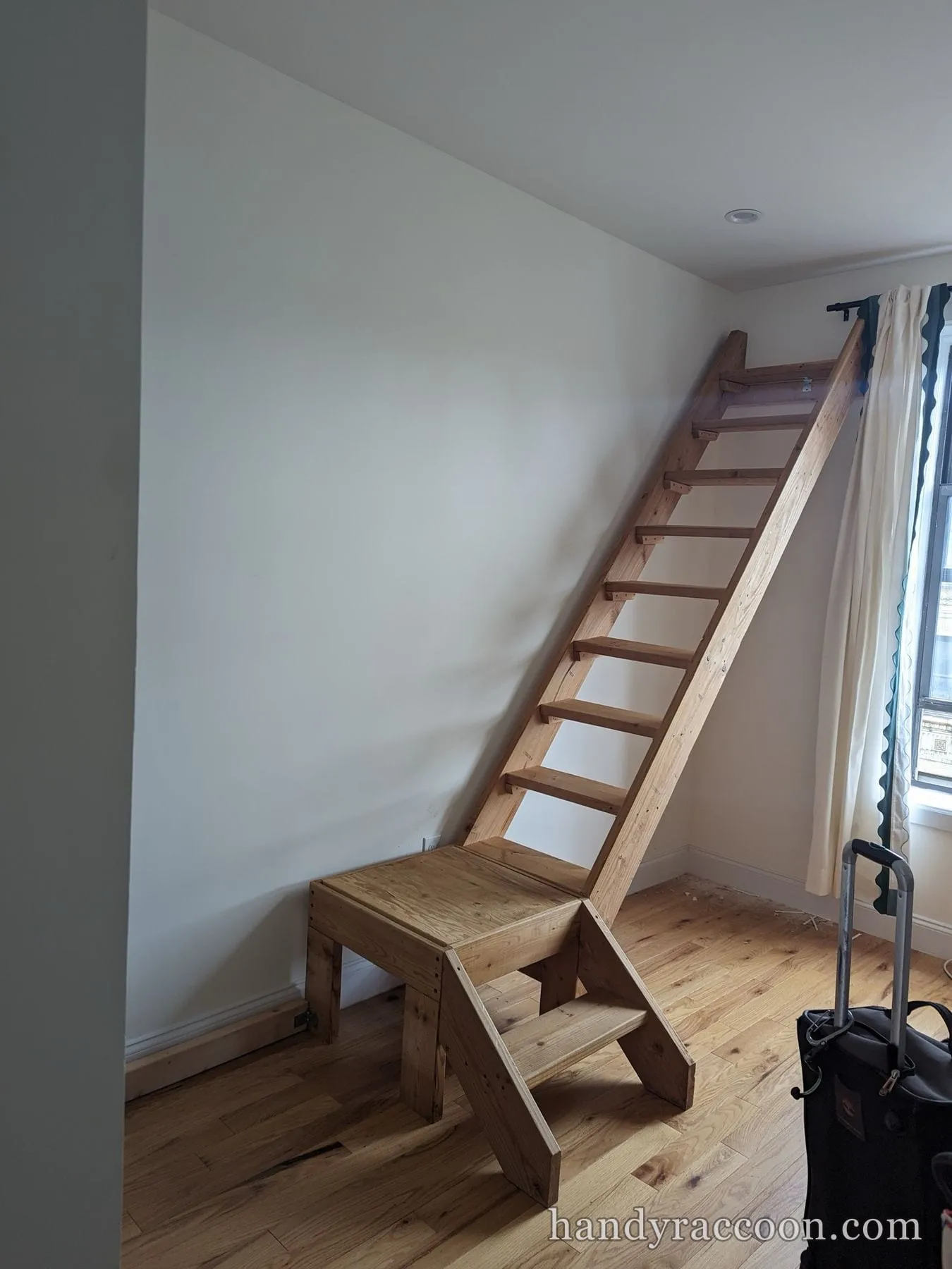 A tall custom pine loft ladder with an attached wide step platform against a white wall.