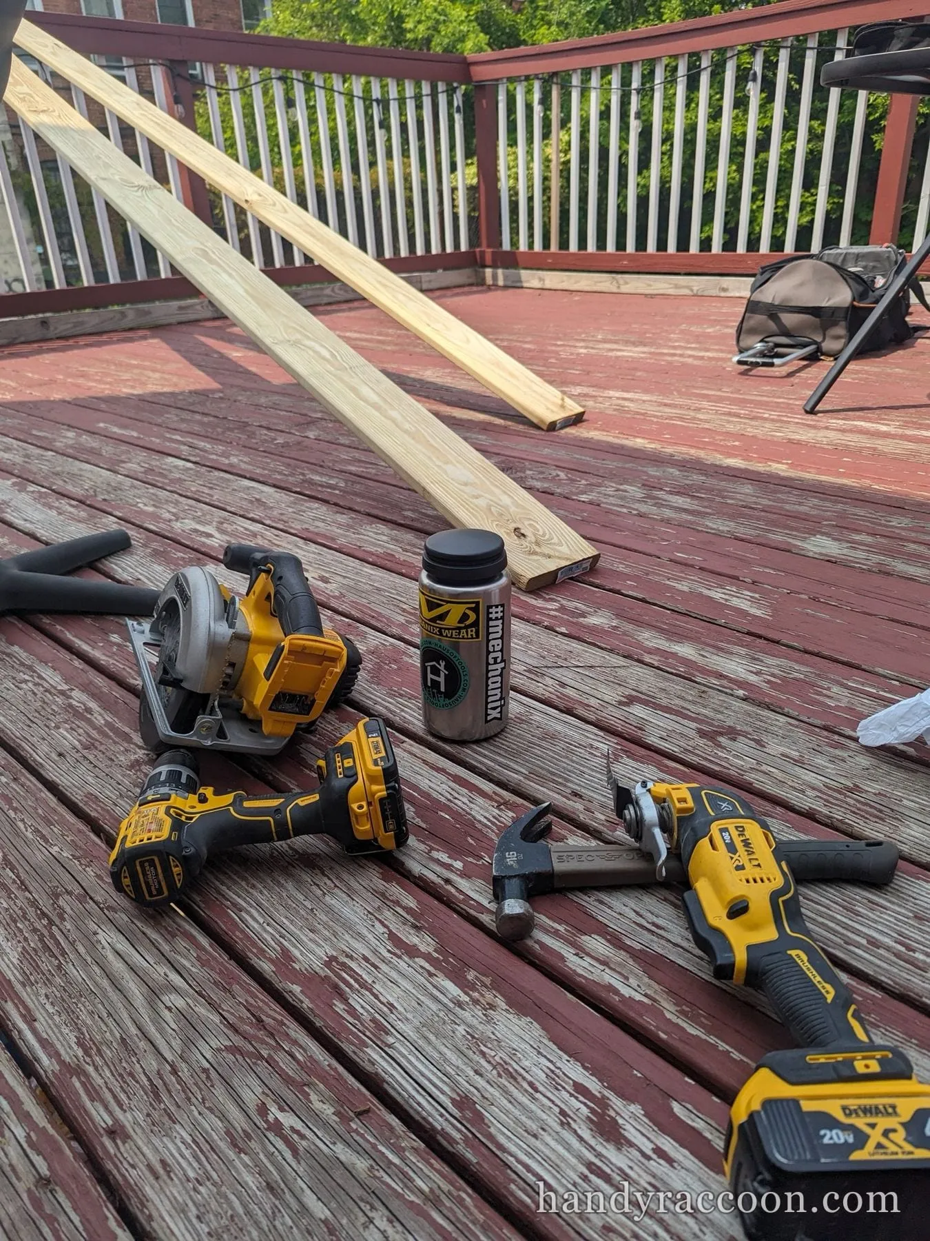 A circular saw, drill, grinder, hammer and two boards laid out on a weathered red deck.