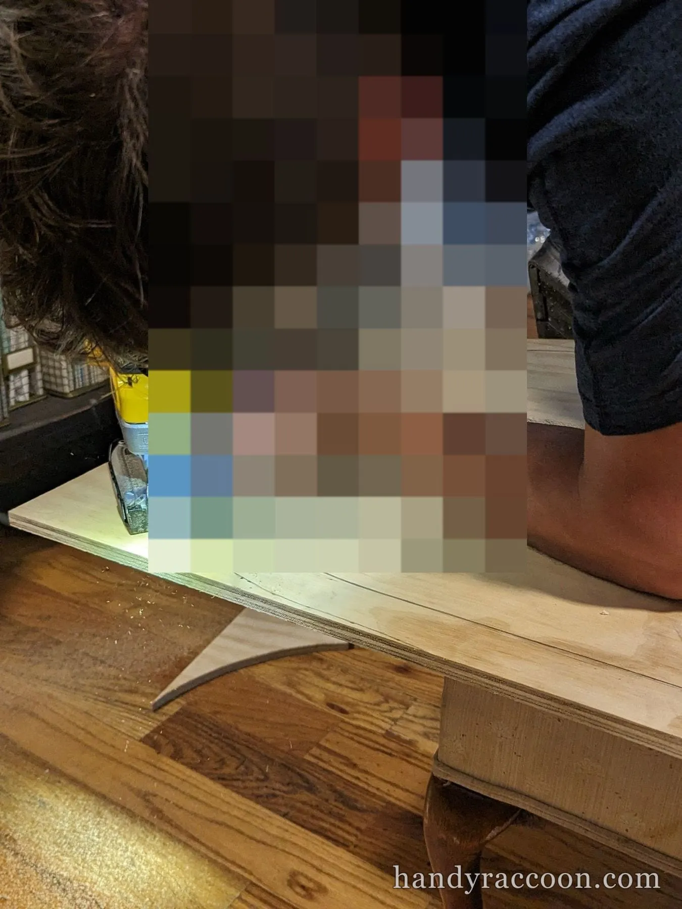 A person bent over guiding a lit cordless cutting tool along a curved line in plywood.